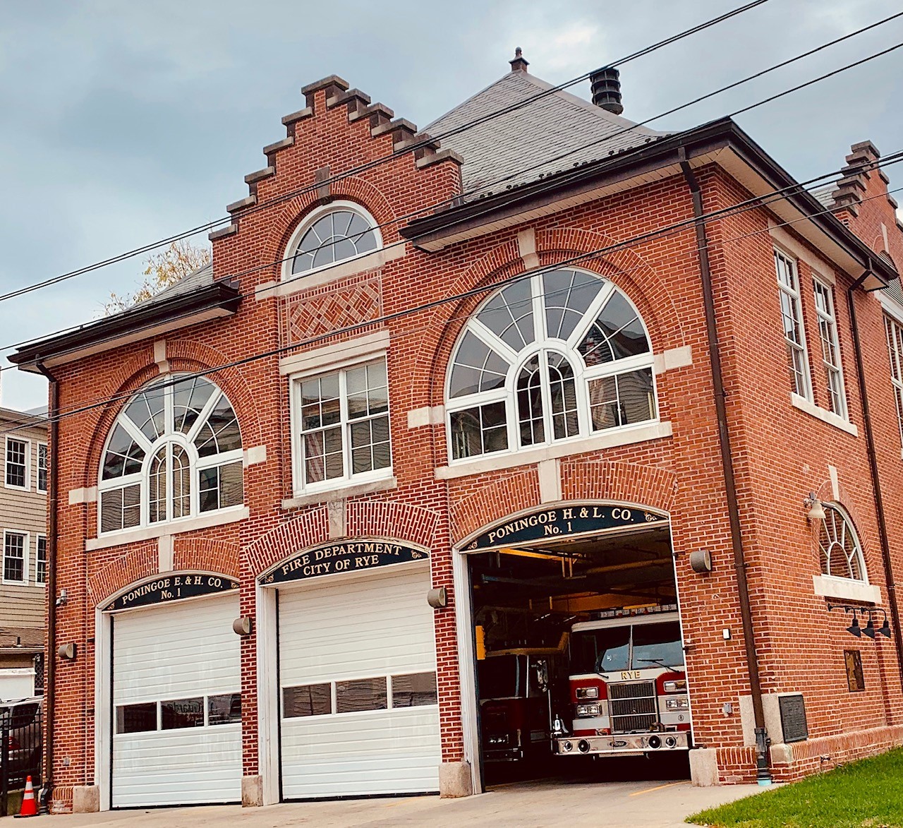 Historic red-brick firehouse with open apparatus bay and fire truck inside.