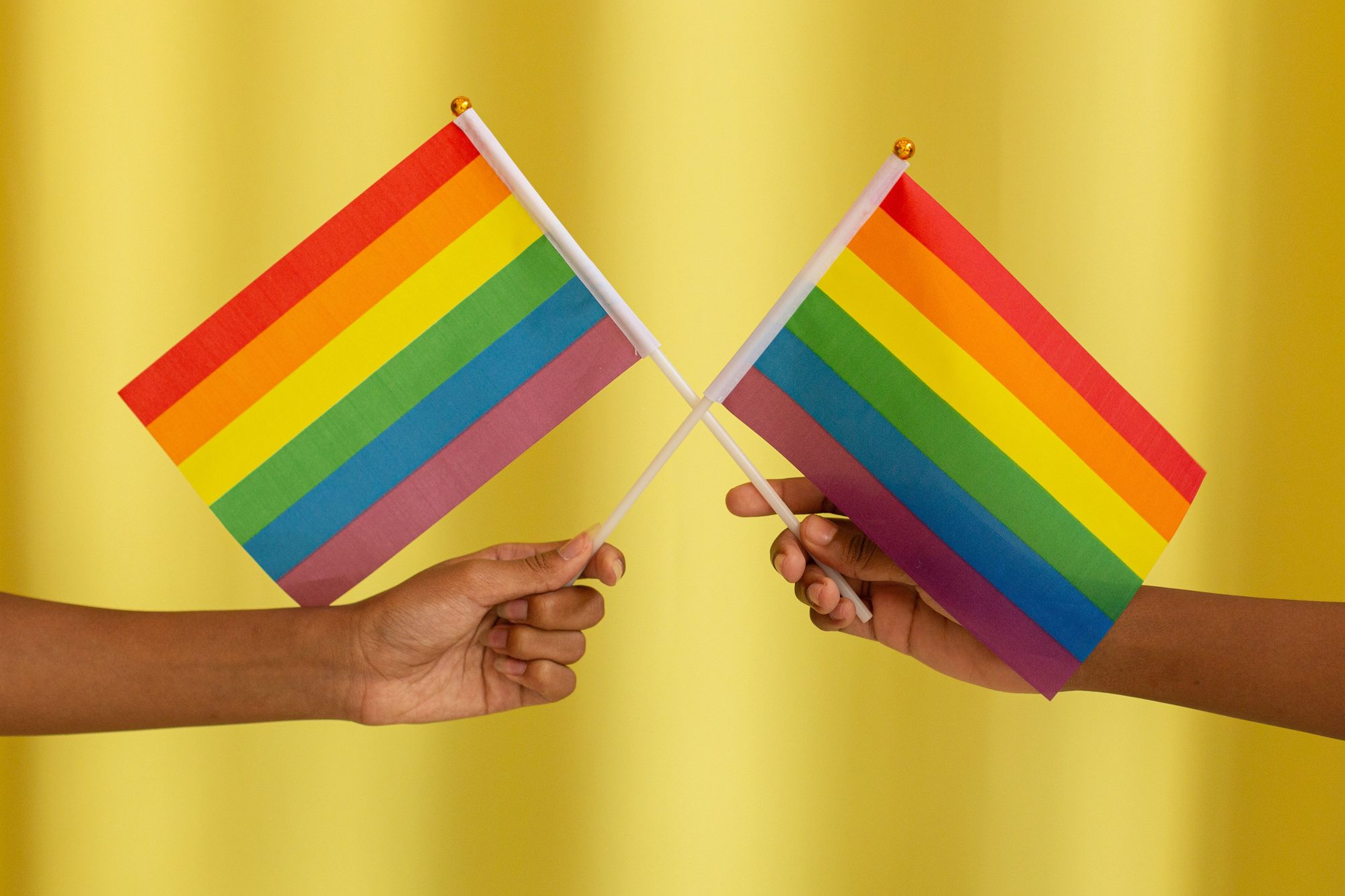 Two hands holding rainbow LGBT pride flags crossed together symbolizing unity and celebration.