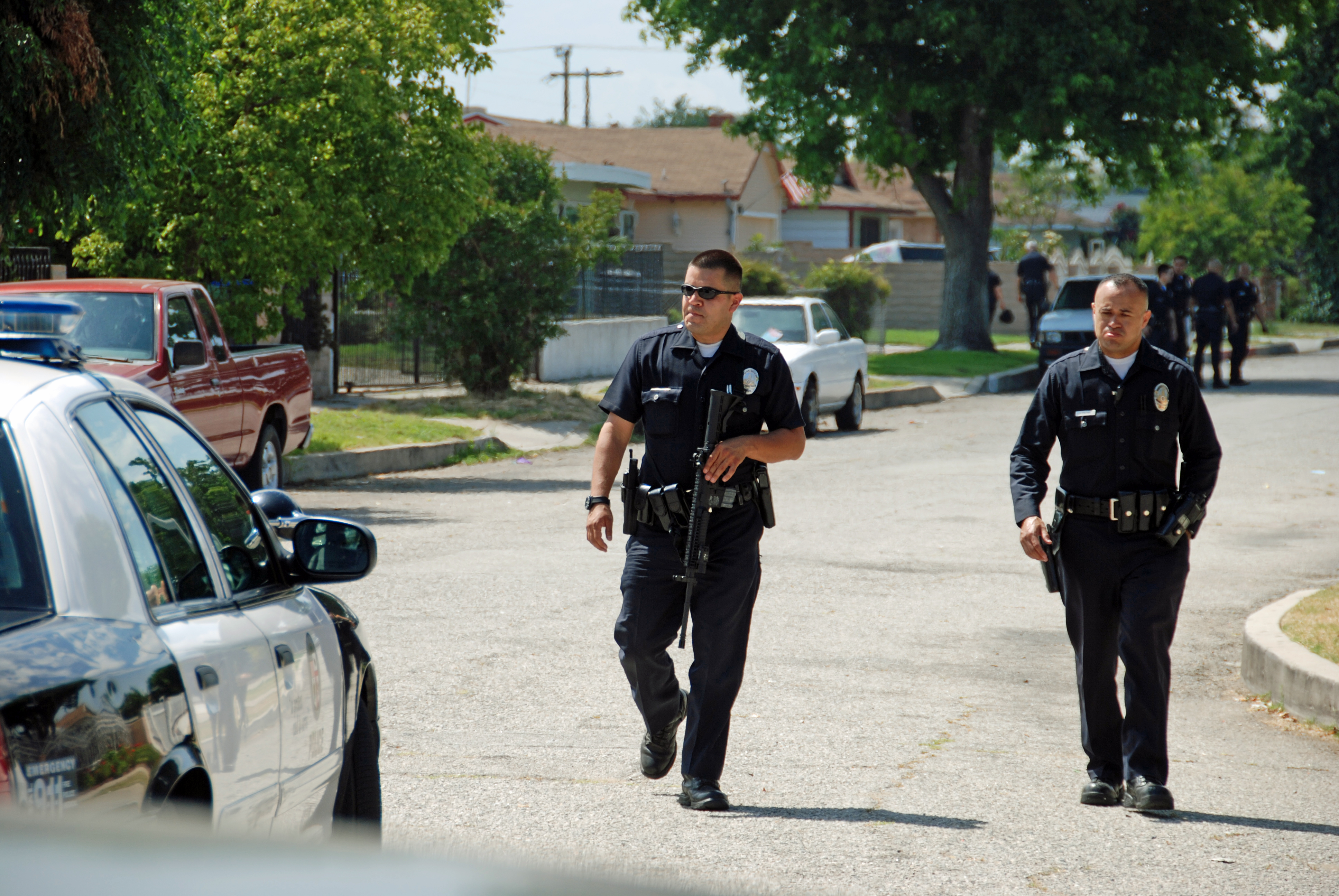 Two uniformed police officers walk toward a patrol car on a residential street.