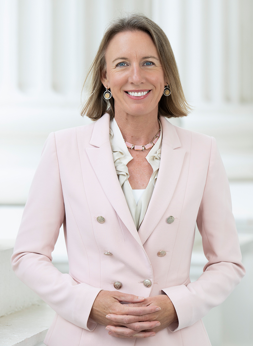 Woman in a light pink blazer smiling in front of white columns.