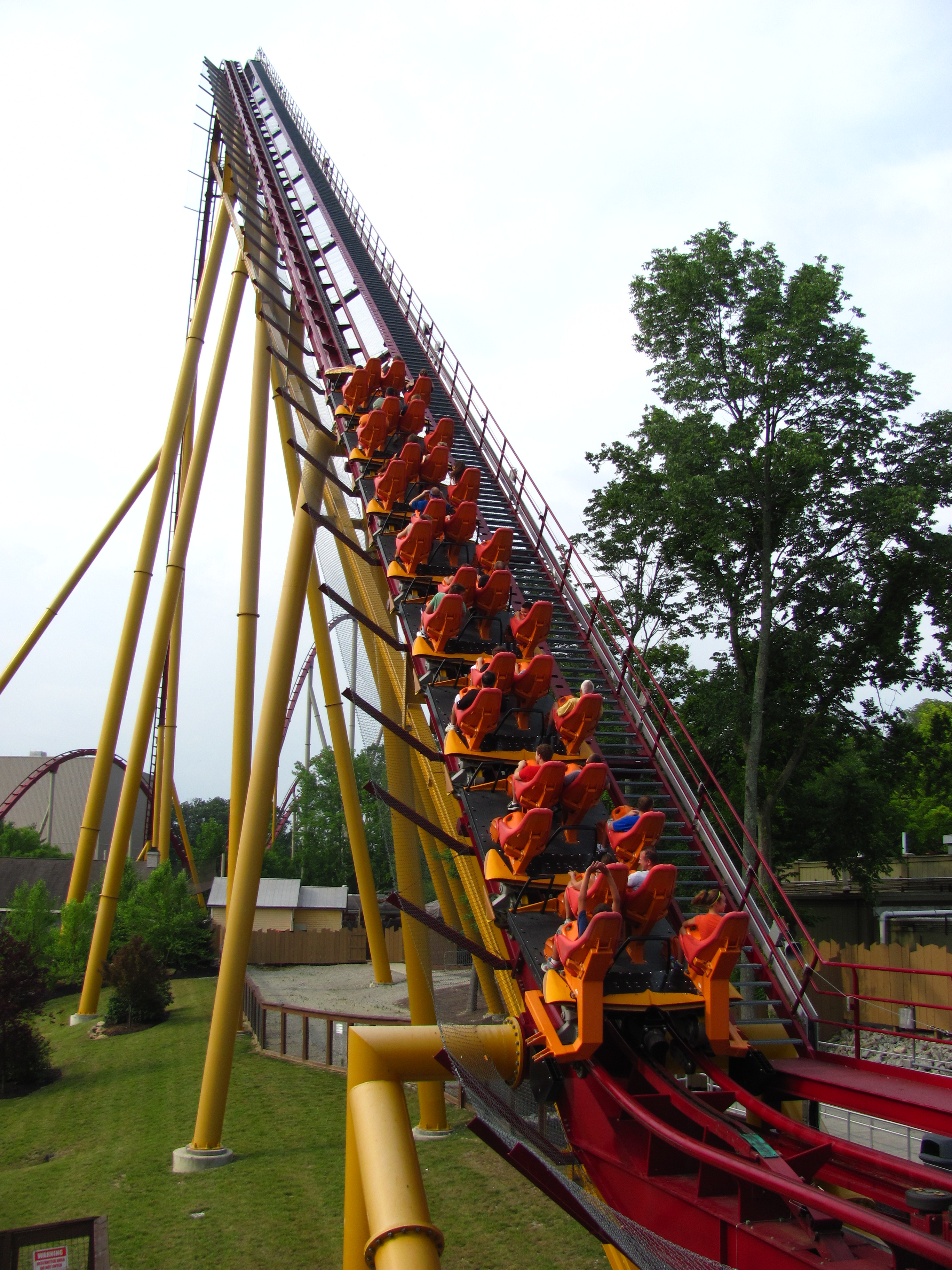 Roller coaster train with riders ascending a steep yellow lift hill.