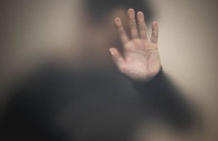 A blurred figure with one open hand extended toward the camera, palm facing outward.