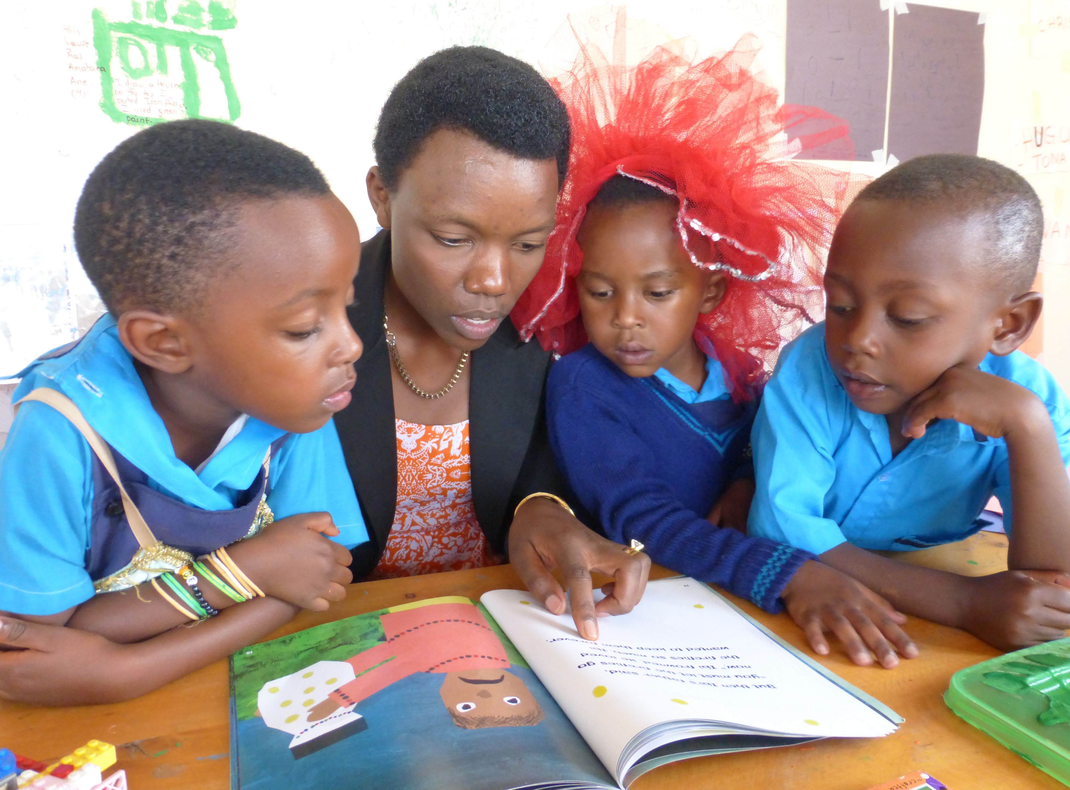An adult reads a picture book aloud to three young children at a table.