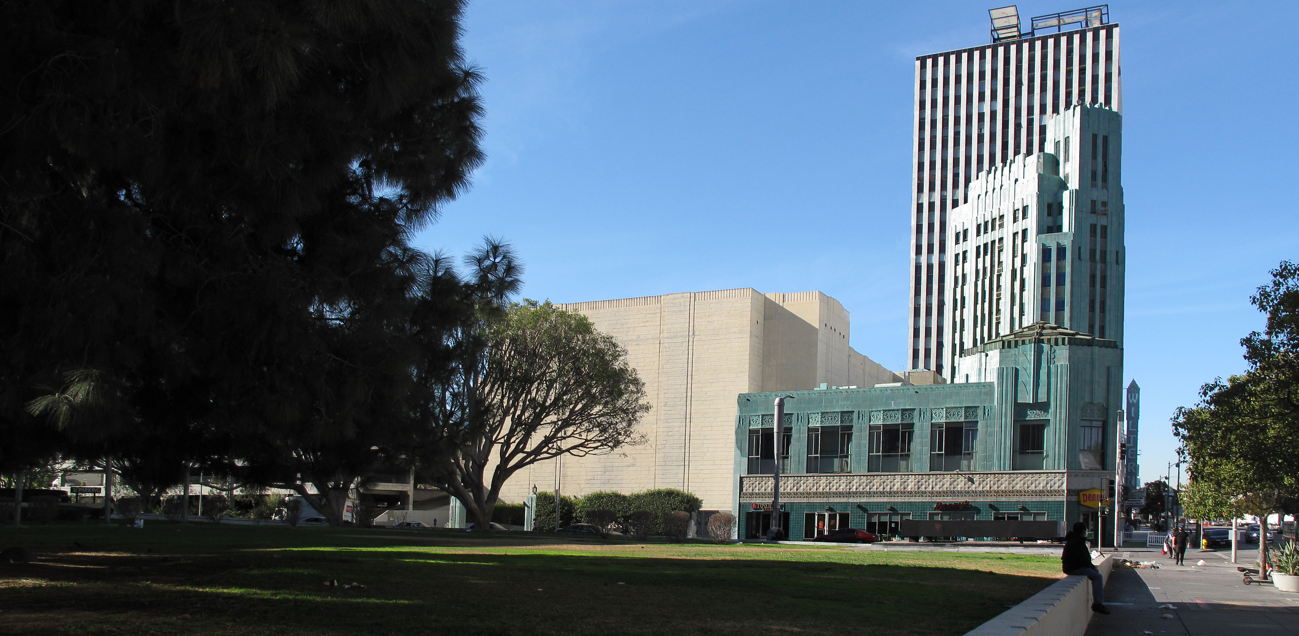 Green lawn with mature trees along Wilshire Boulevard, Wiltern Theatre visible behind.