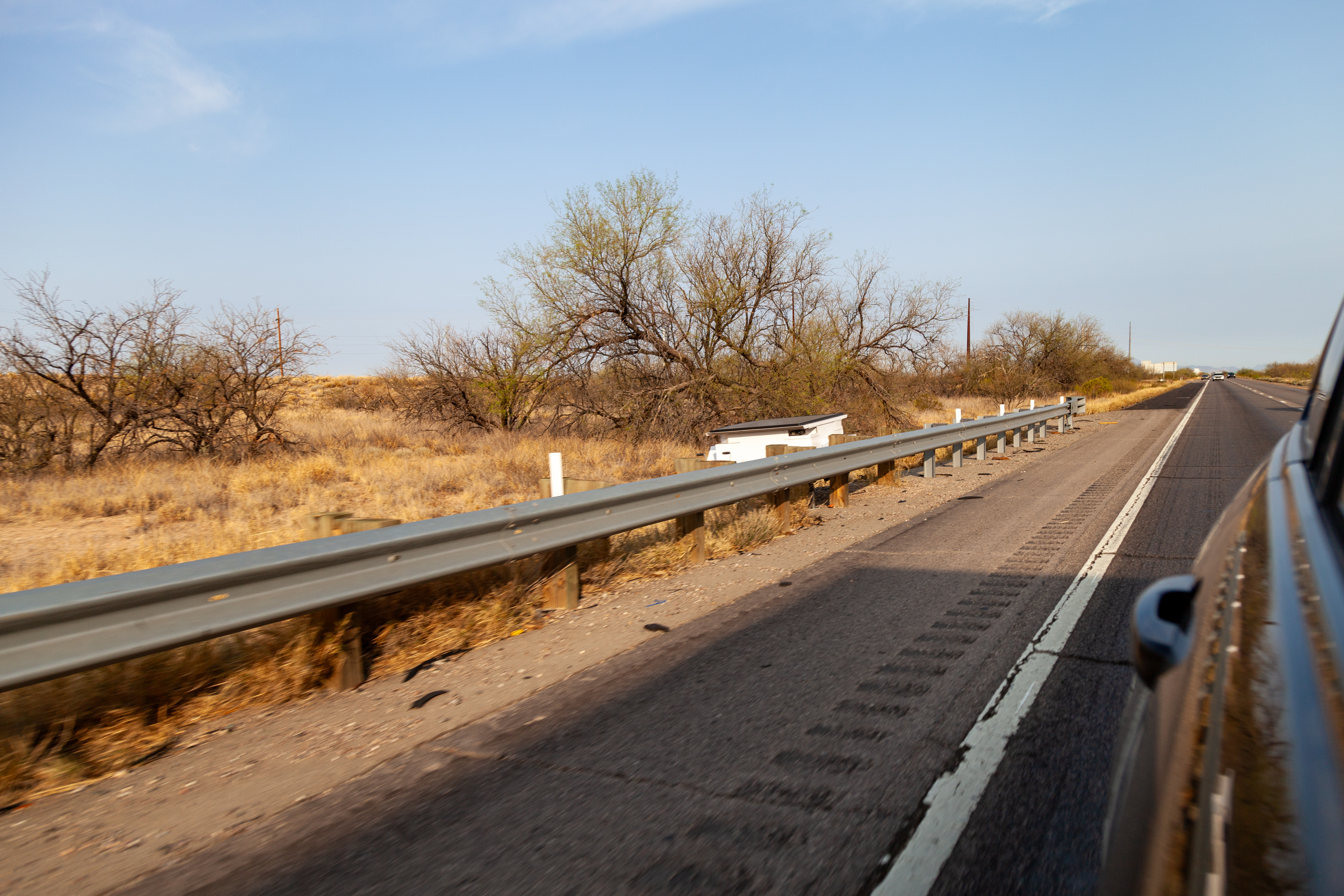 An ALPR camera on a post along a highway shoulder with scrubland behind it.