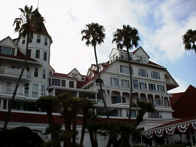 Victorian resort building with red conical turrets and white wooden facade surrounded by tall palm trees.