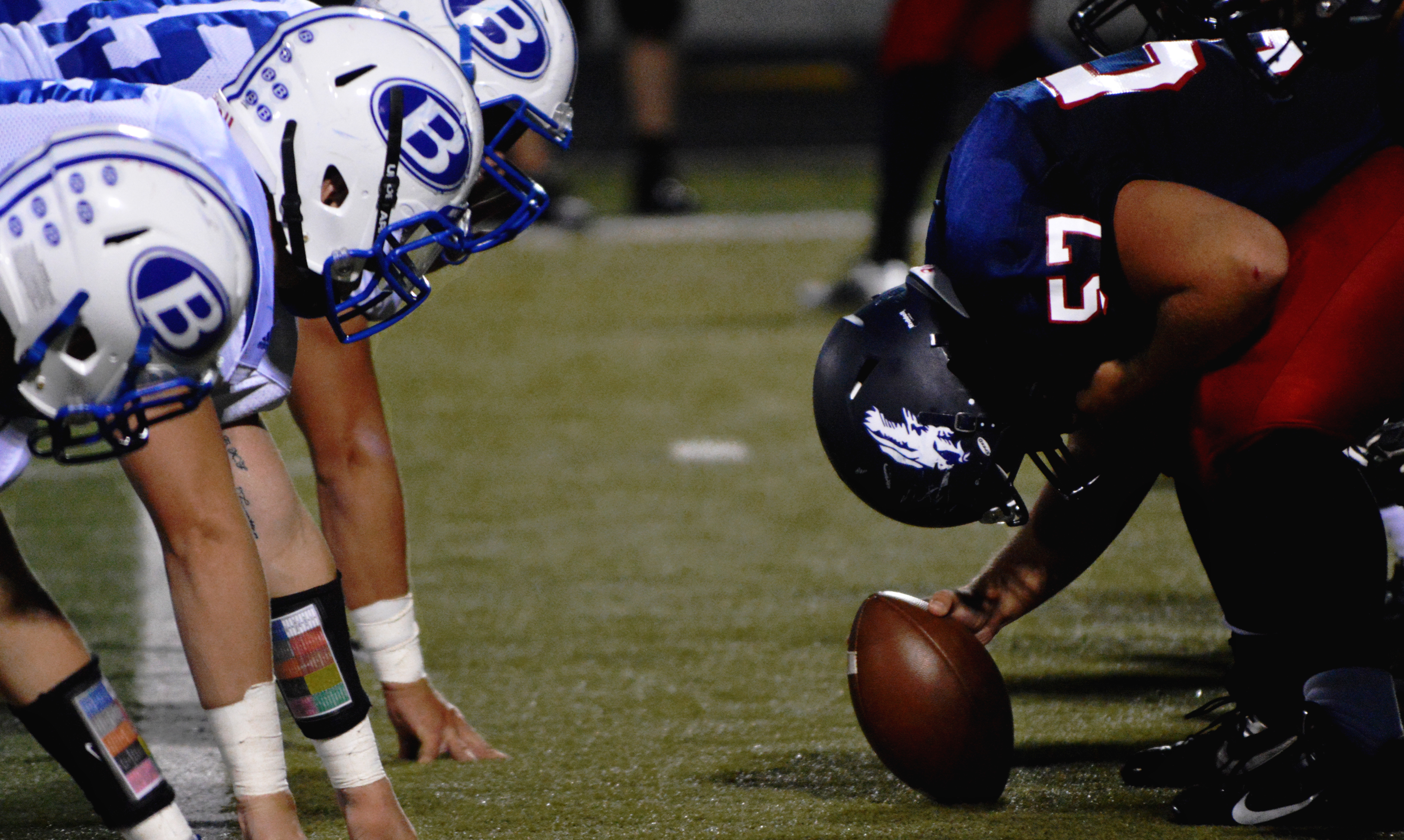 Two football teams lined up at the line of scrimmage under stadium lights.