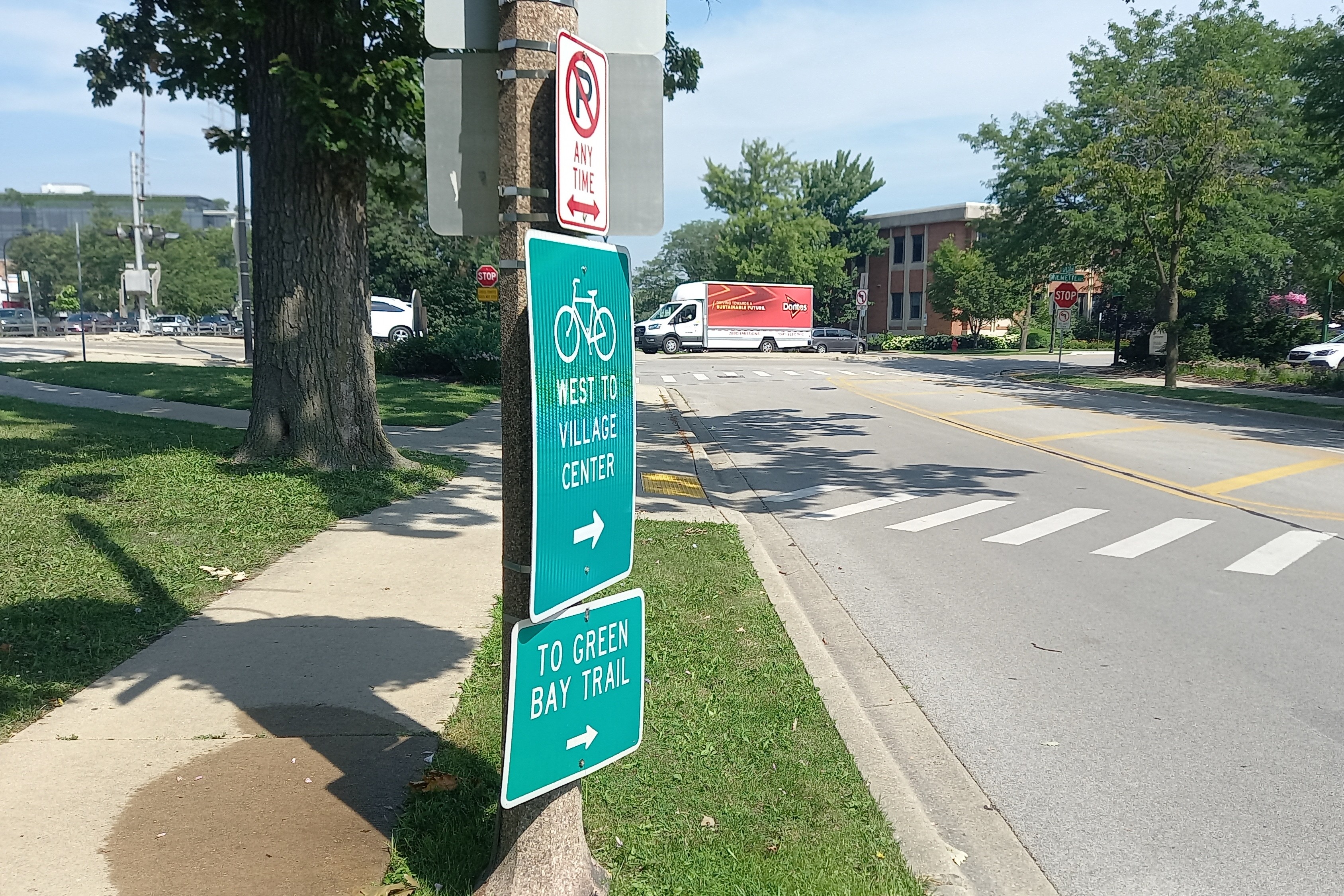 Green bicycle guide signs on a pole directing cyclists to a village center and trail.