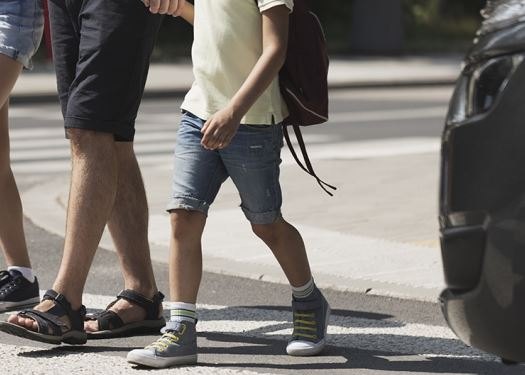 Adult and child crossing a street at a marked crosswalk, car visible nearby.