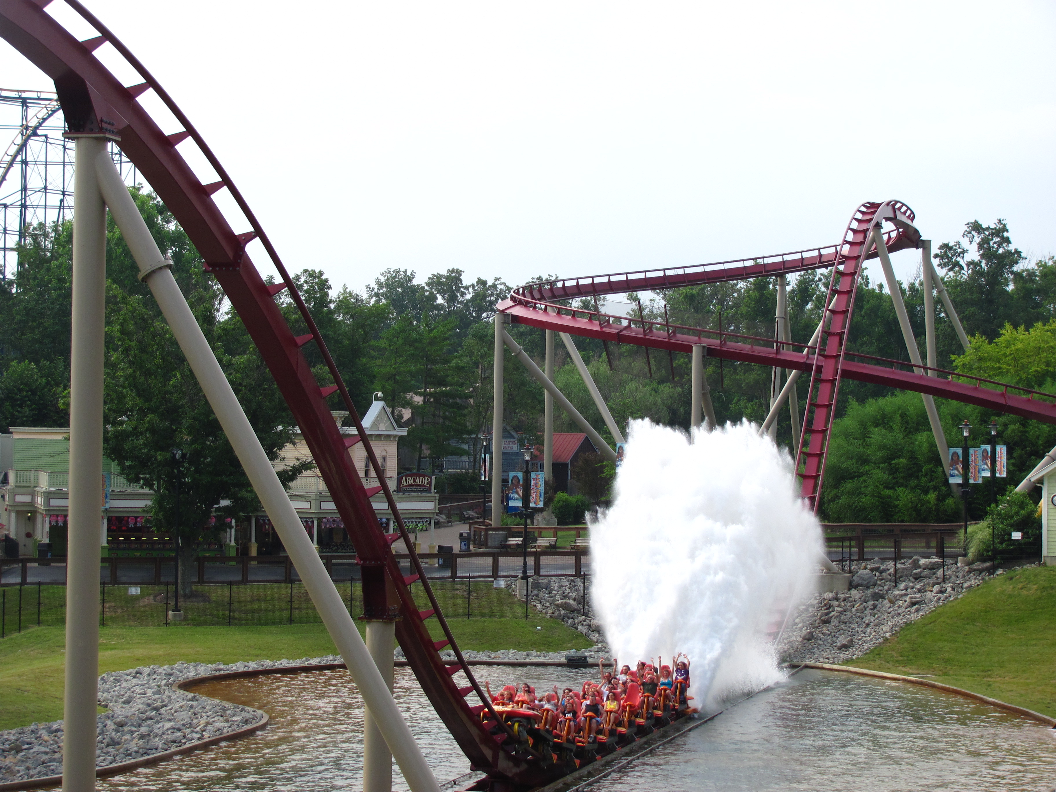 Roller coaster train splashing through a water trough on a red-tracked ride.