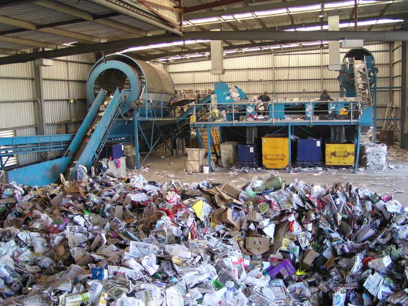 Interior of a recycling facility with piles of mixed materials and conveyor sorting equipment.