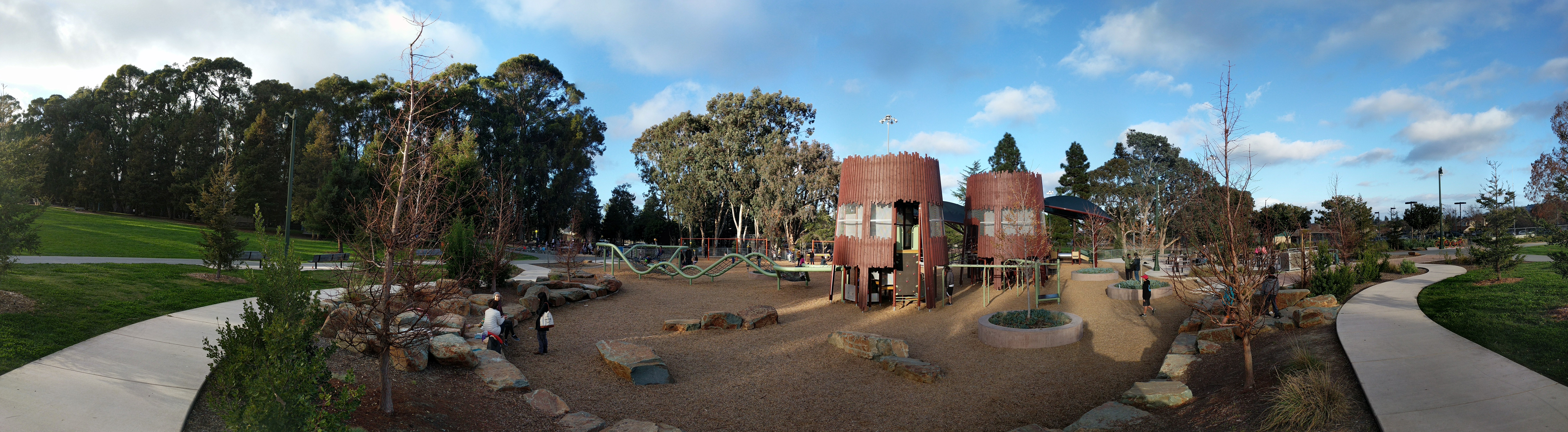 Wide view of a public park playground with cylindrical tower structures and pathways.