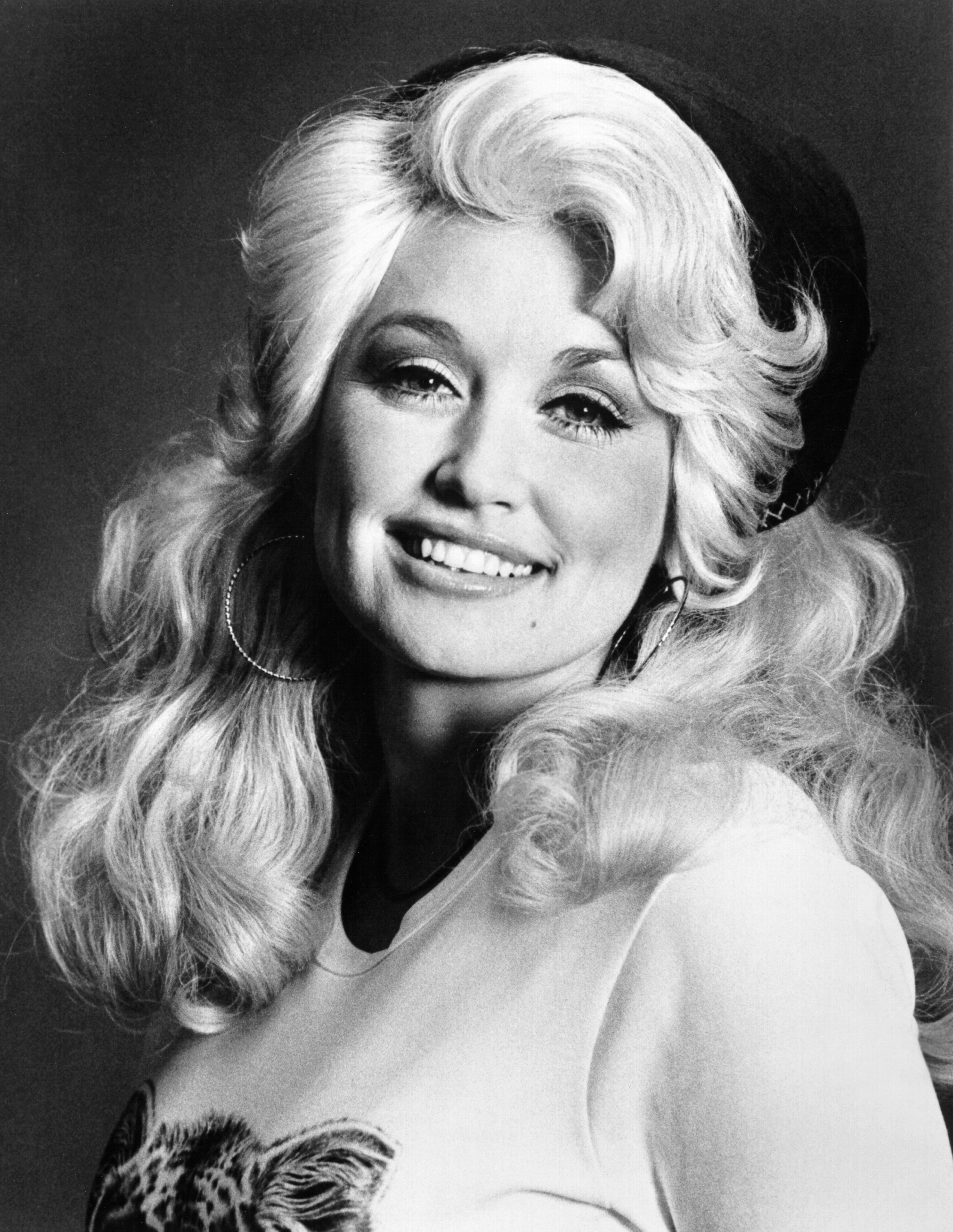 Black-and-white portrait of a smiling woman with voluminous blonde hair.