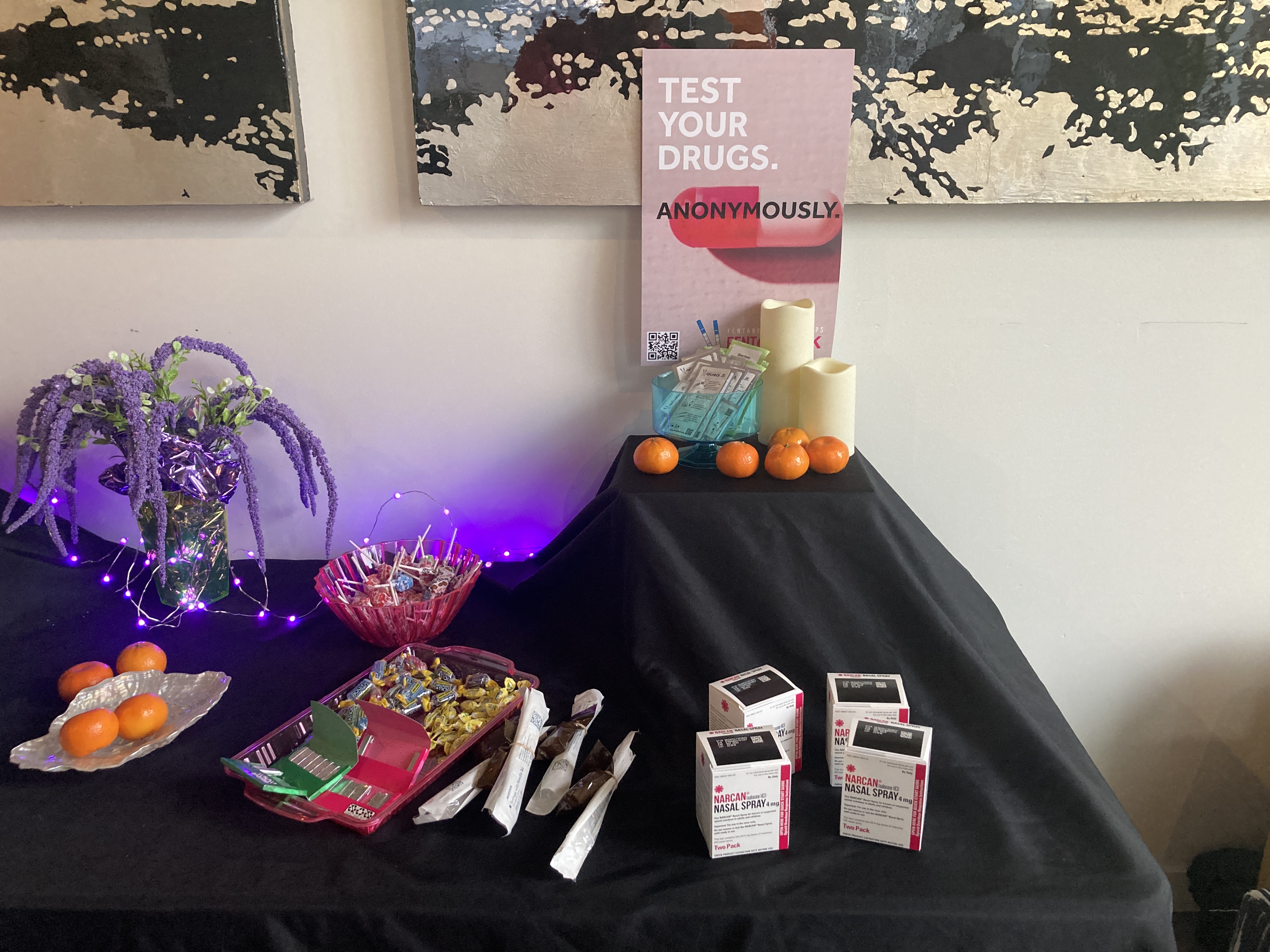 Table with Narcan spray boxes, naloxone syringes, and fentanyl test strips on display.