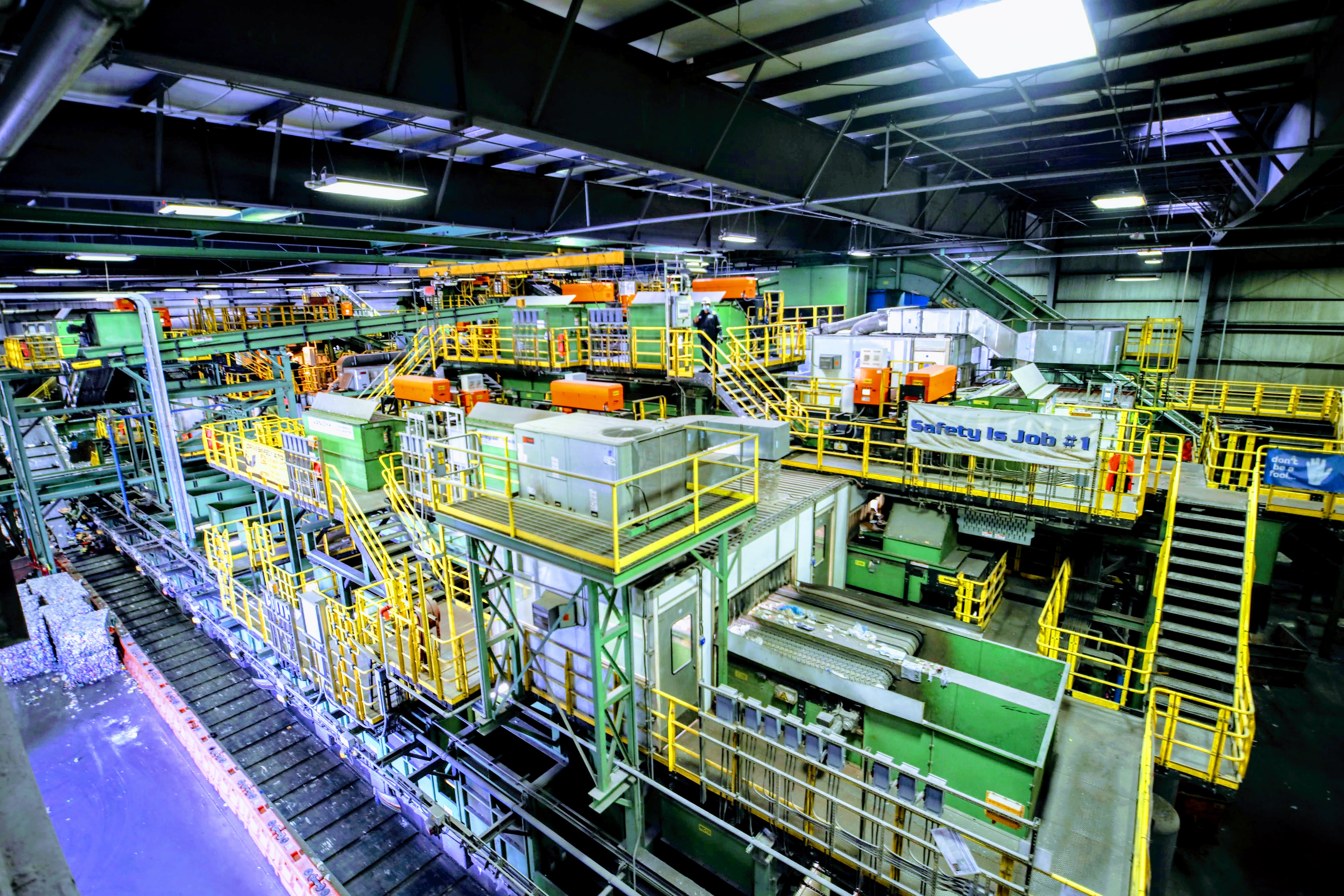 Green industrial sorting machines and conveyor belts inside a large recycling facility.