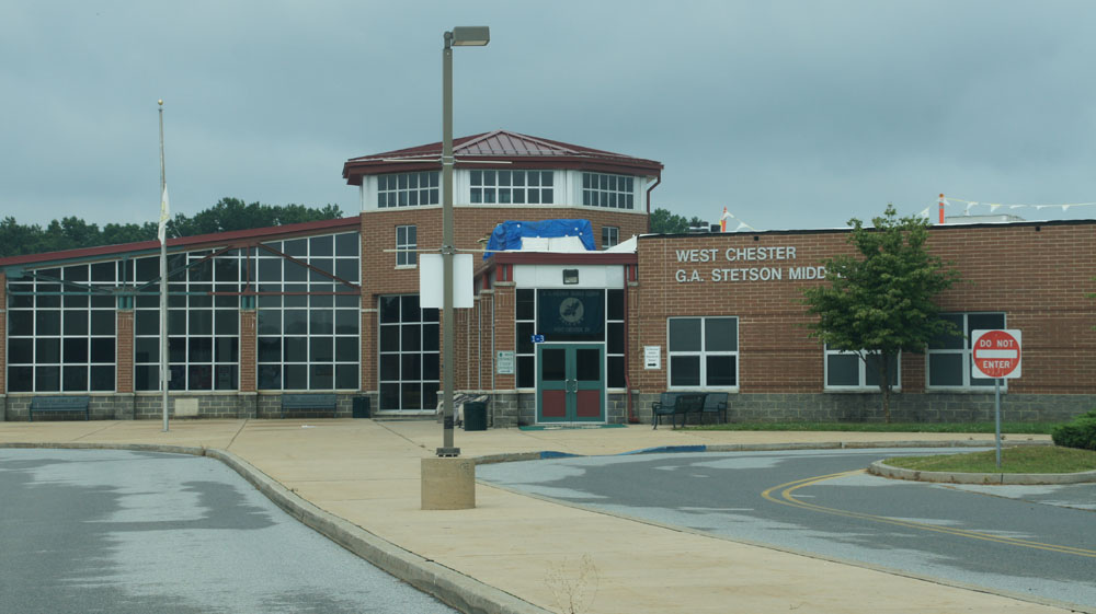 Brick school building with large glass windows and a red-roofed central tower.