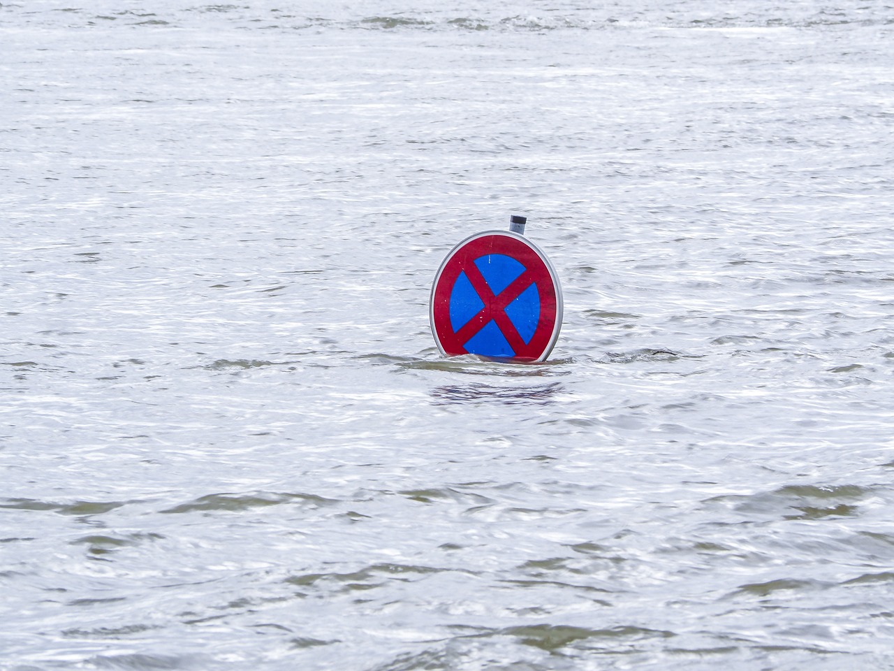 A "no stopping" traffic sign stands partially submerged in floodwater, its base and post underwater.