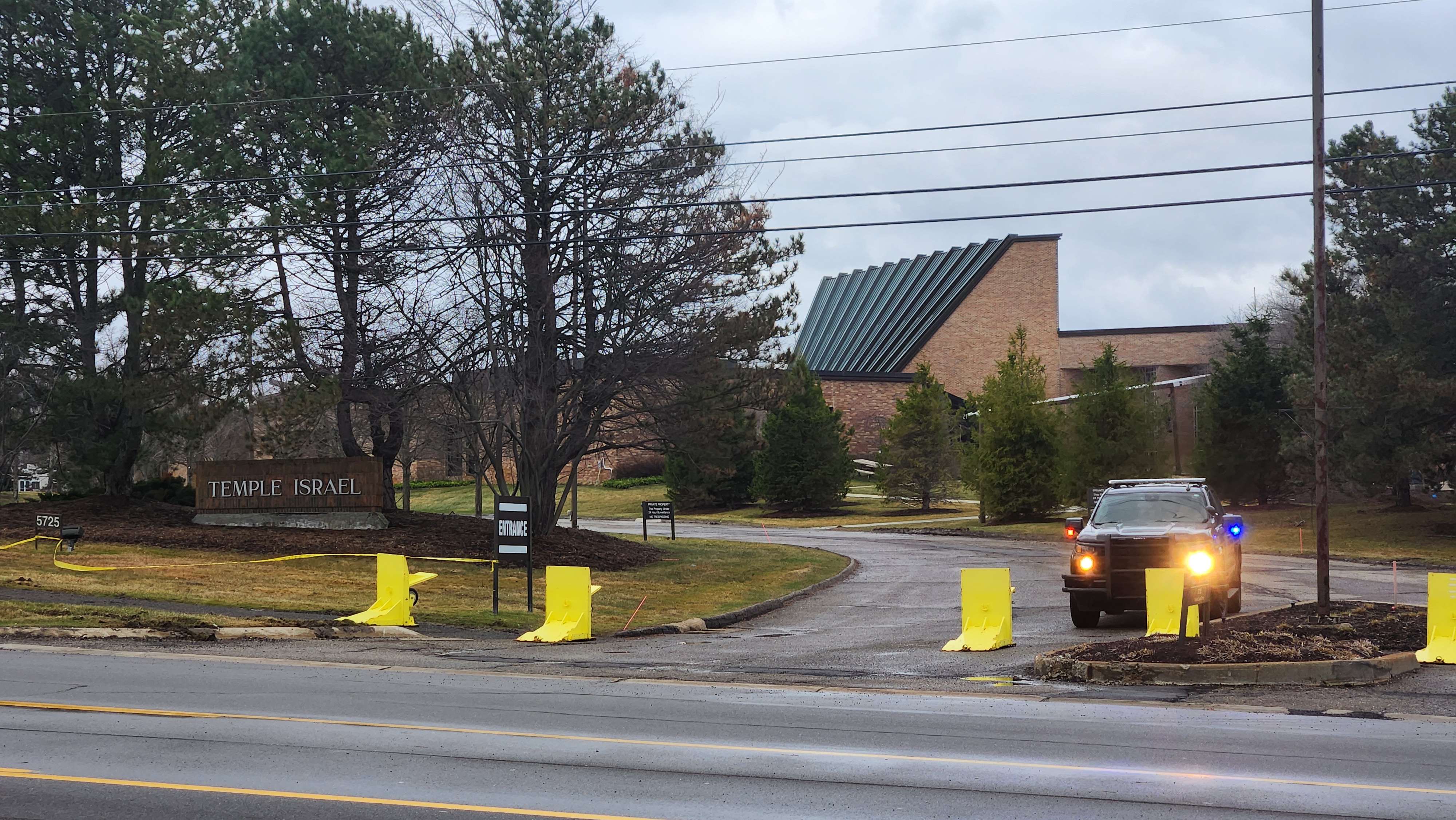 Synagogue entrance with yellow barriers and a police vehicle with emergency lights on.