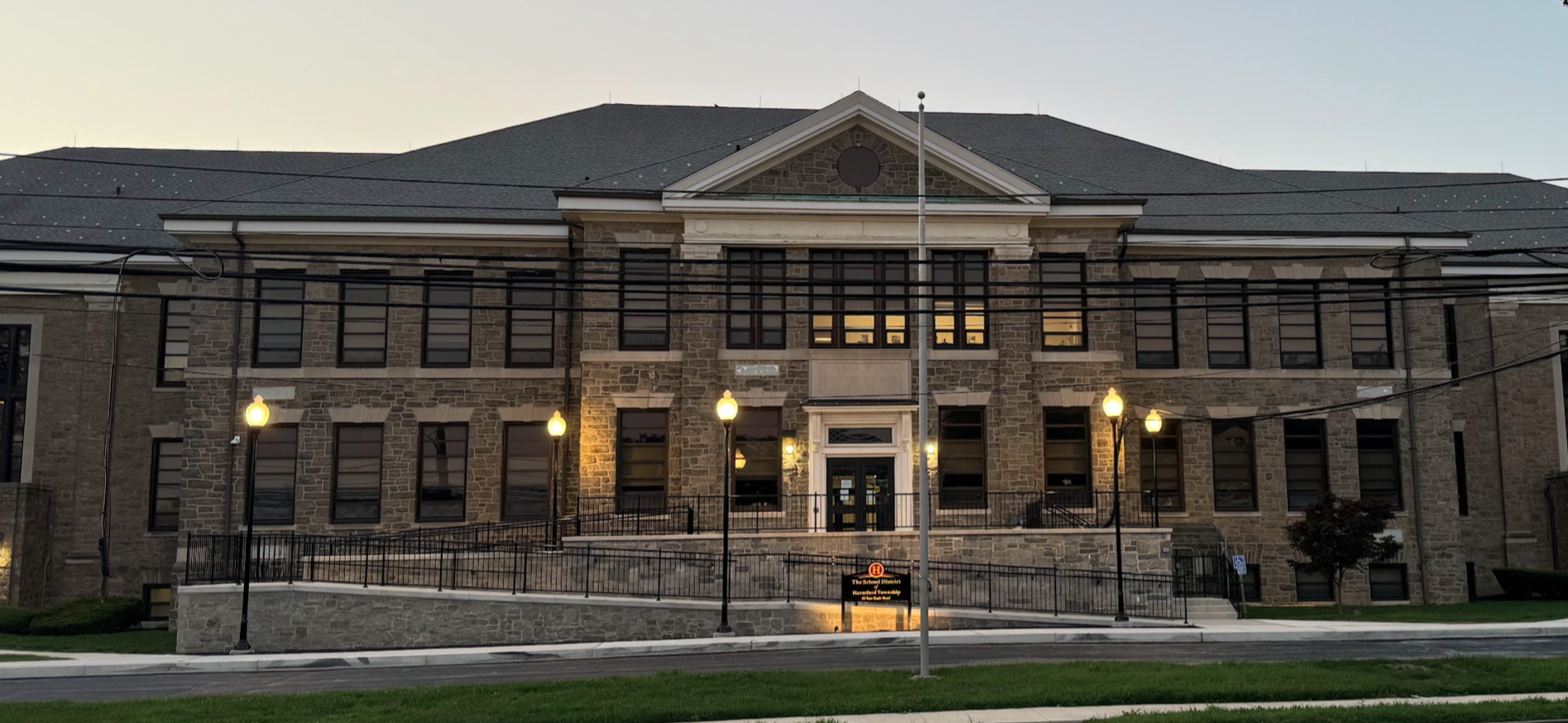 Two-story brick and stone school building at dusk with exterior lights illuminated.