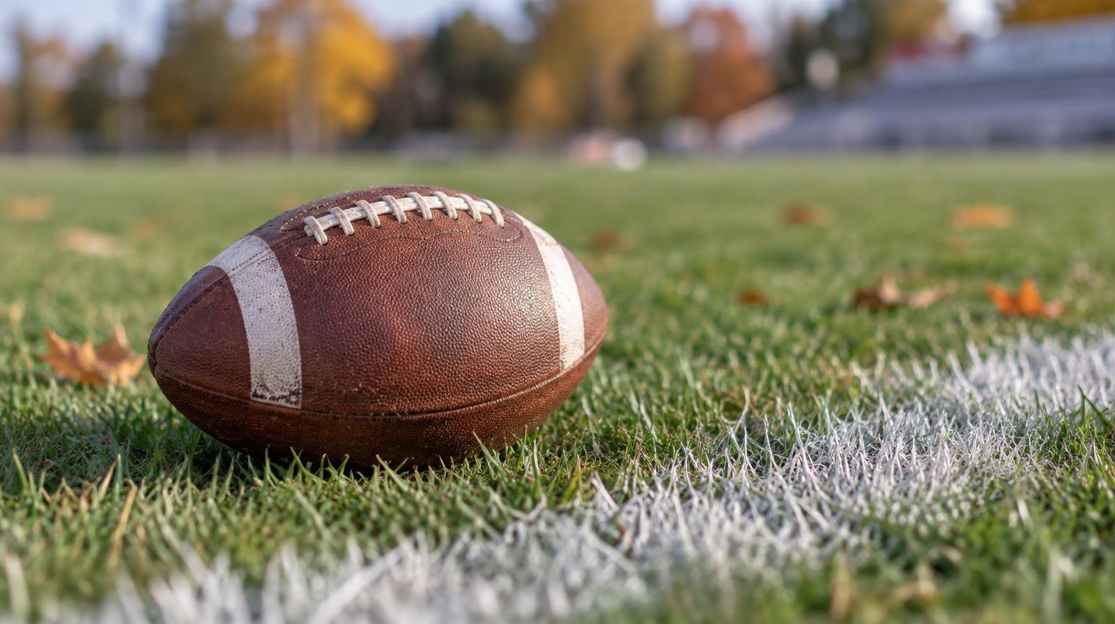 A football resting on green grass next to a white painted yard line.
