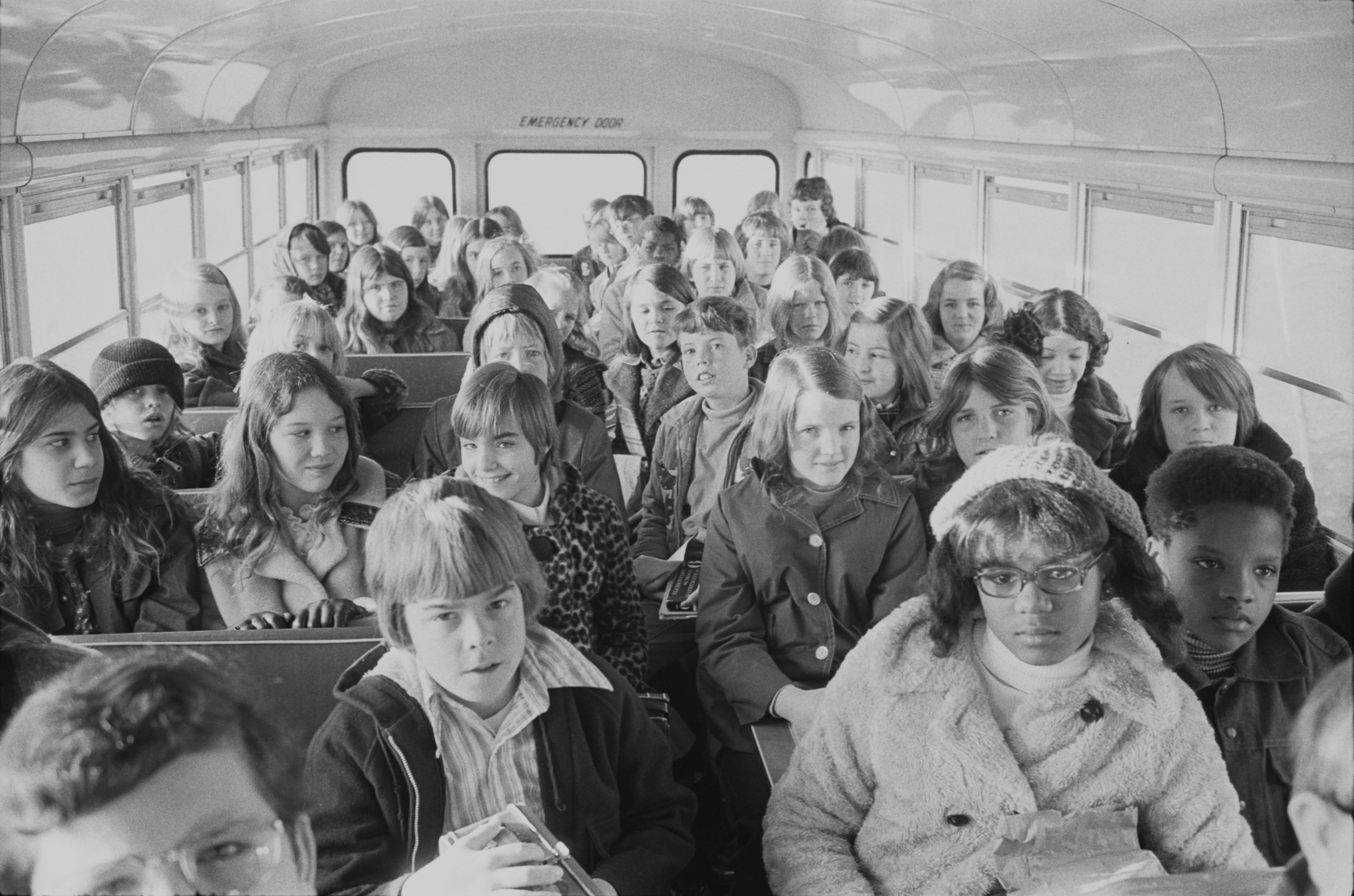 Children of various races seated on a school bus, viewed from the front toward the rear.