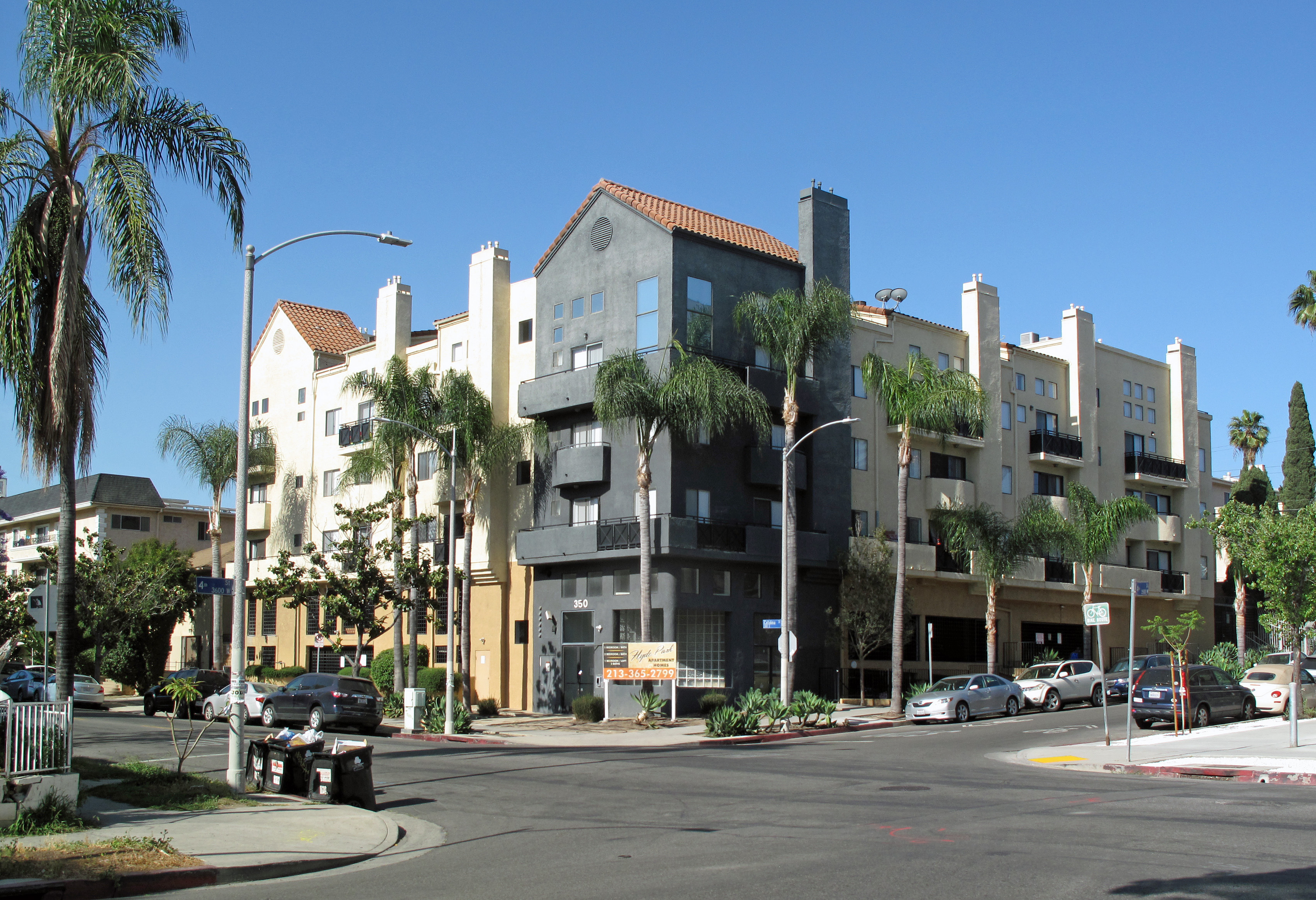 Multi-story apartment building and palm trees at a sunny Koreatown street corner.