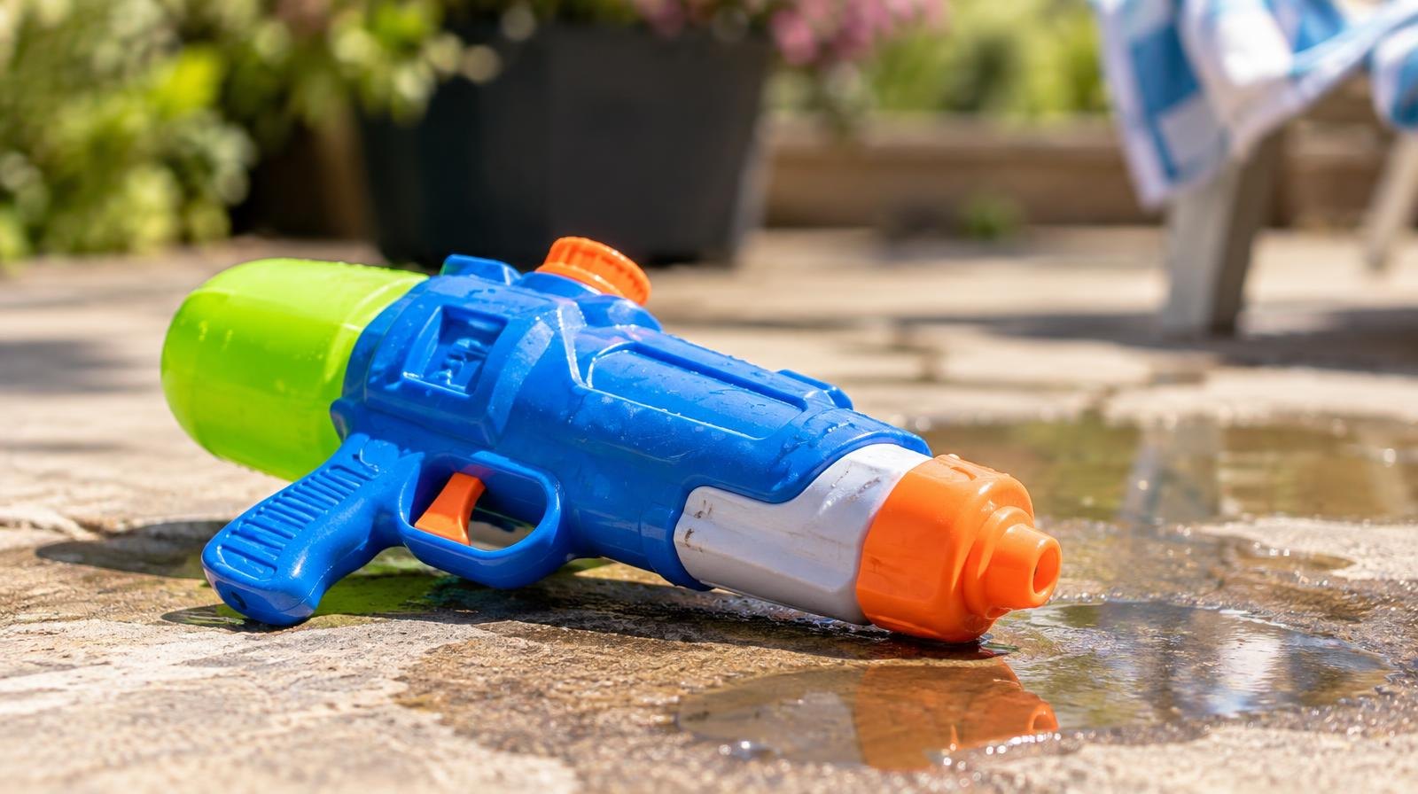 A brightly colored plastic water gun resting on a wet concrete surface in sunlight.
