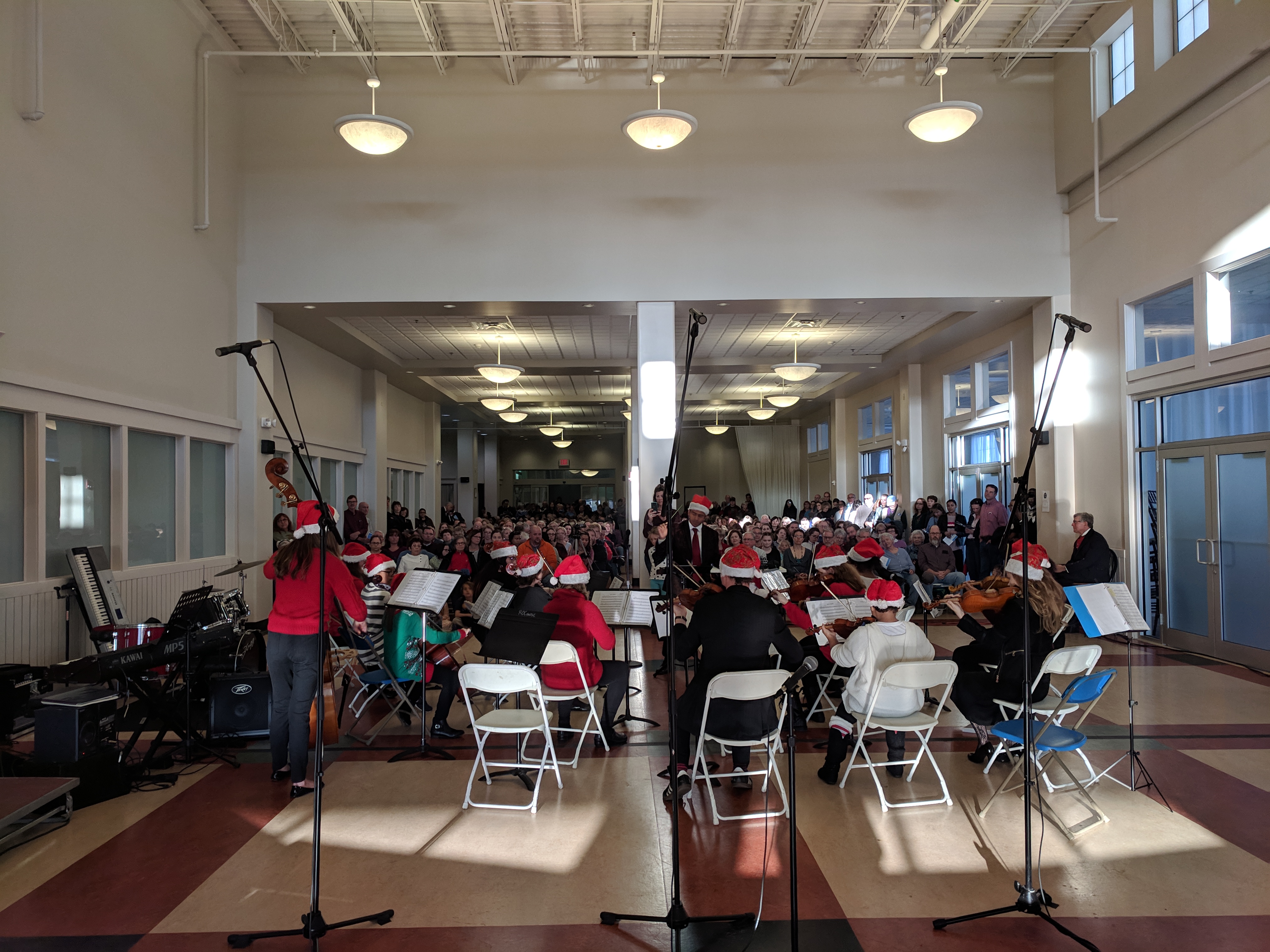 Performers seated at music stands in a large indoor concert hall.