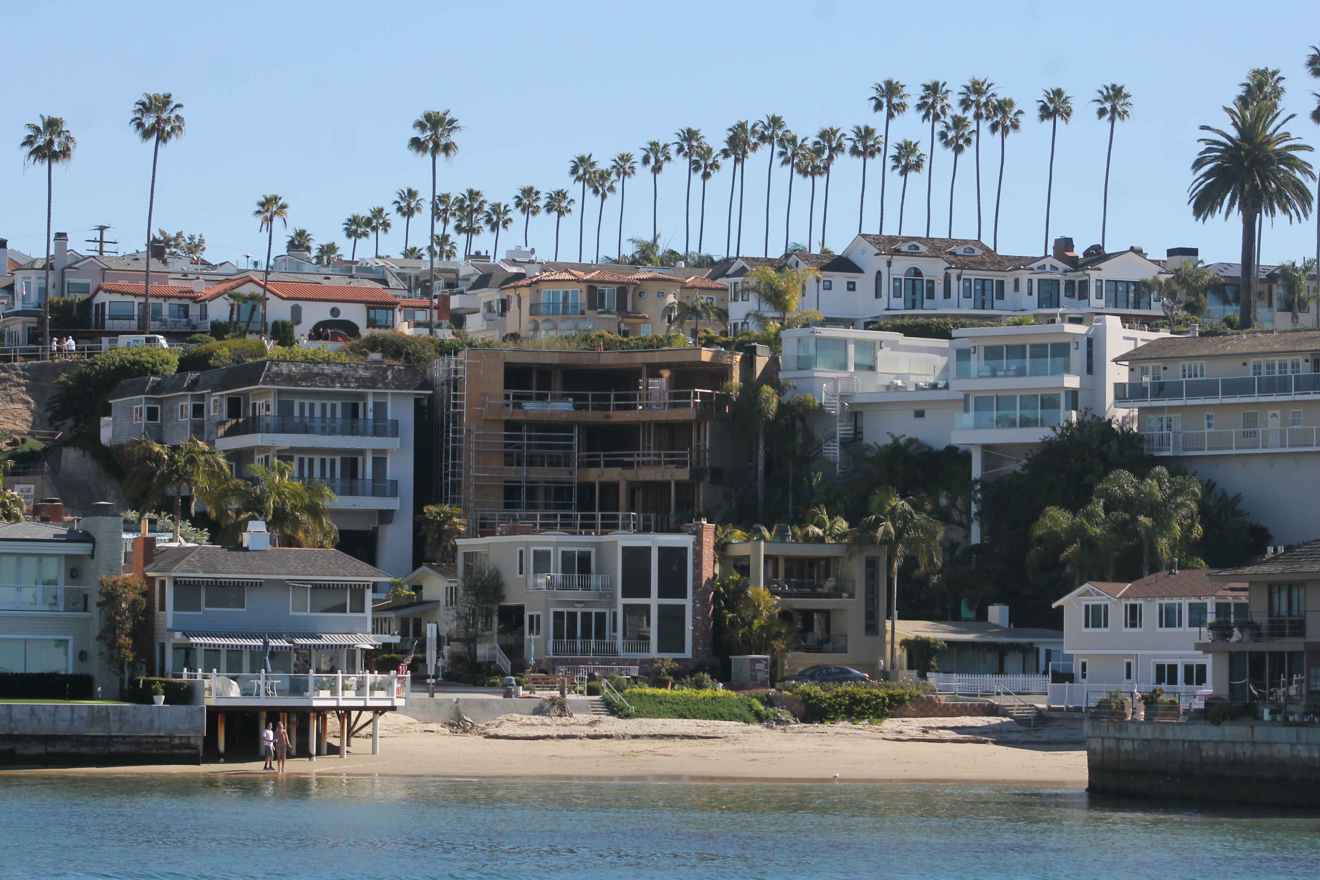 Multi-story beach houses along a sandy waterfront hillside with palm trees in Newport Beach.