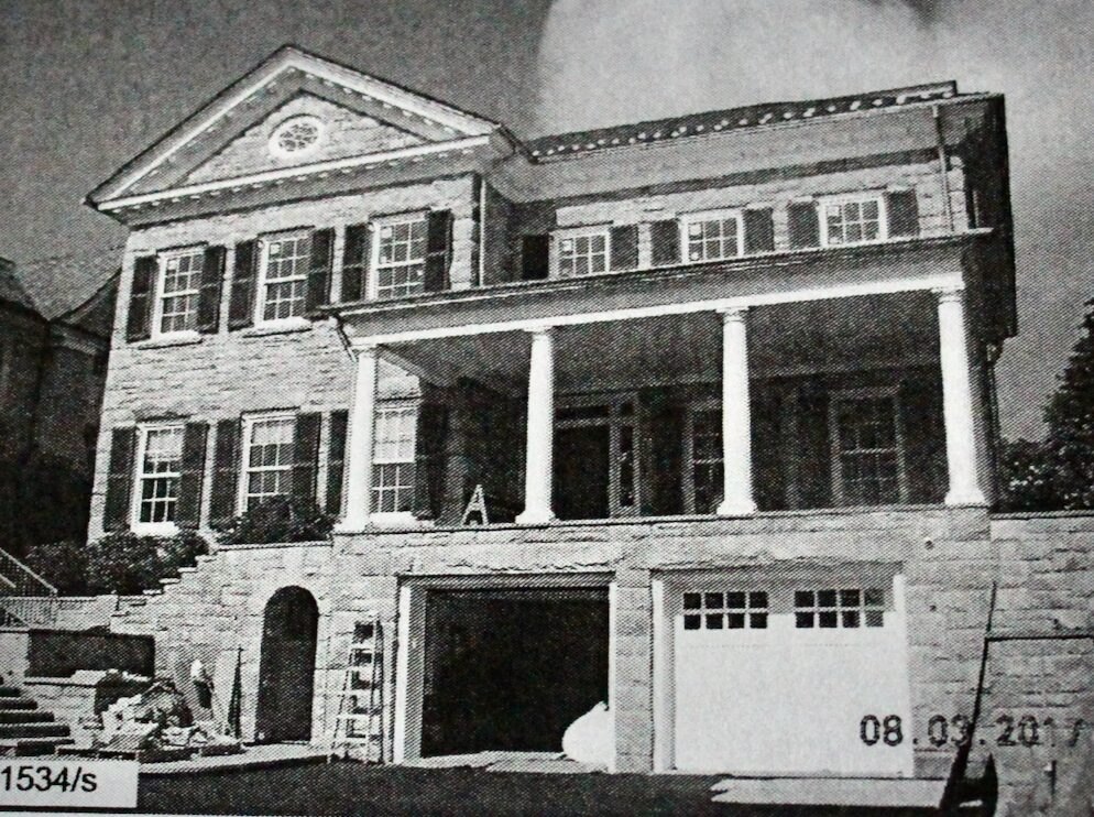 Large two-story colonial stone house with white columns and covered front porch.