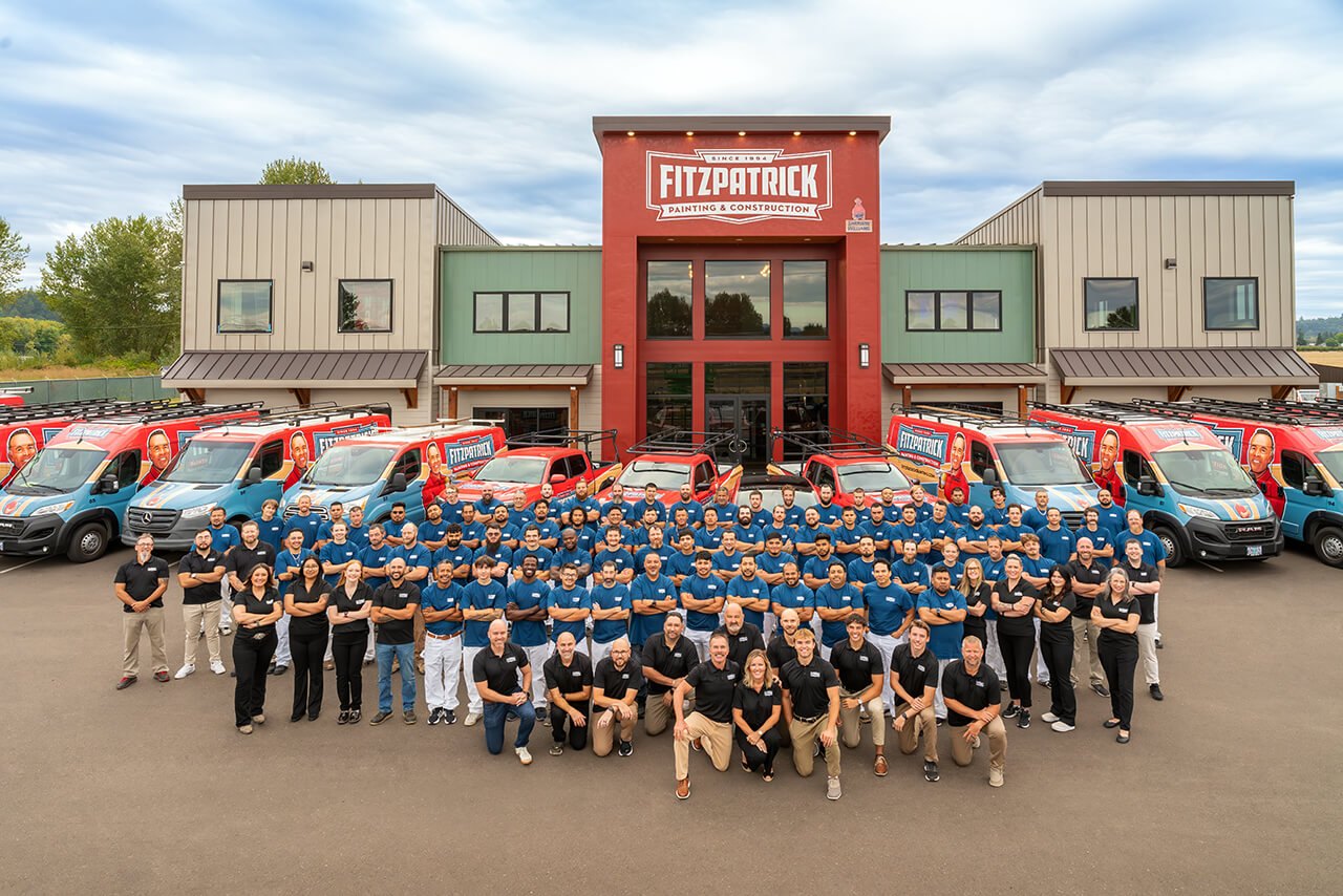 Large group of uniformed employees posing in front of a building with company vans.