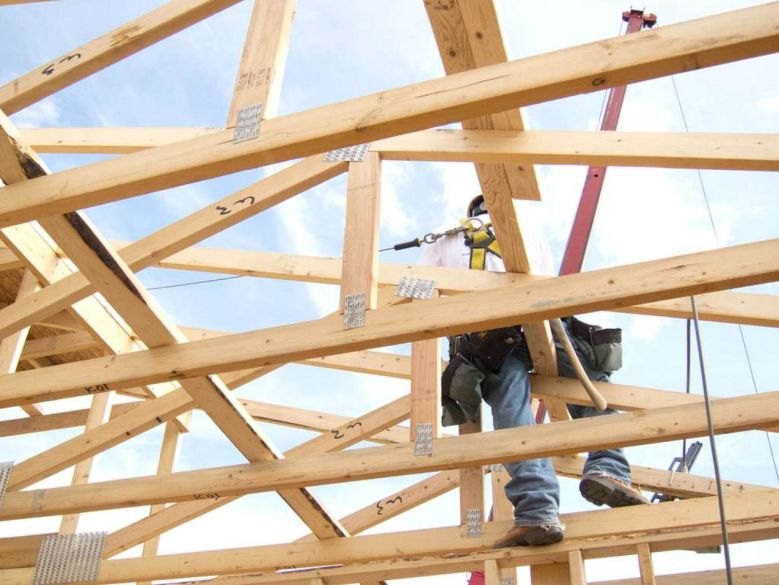 Construction worker standing on wooden roof trusses of a home under construction.