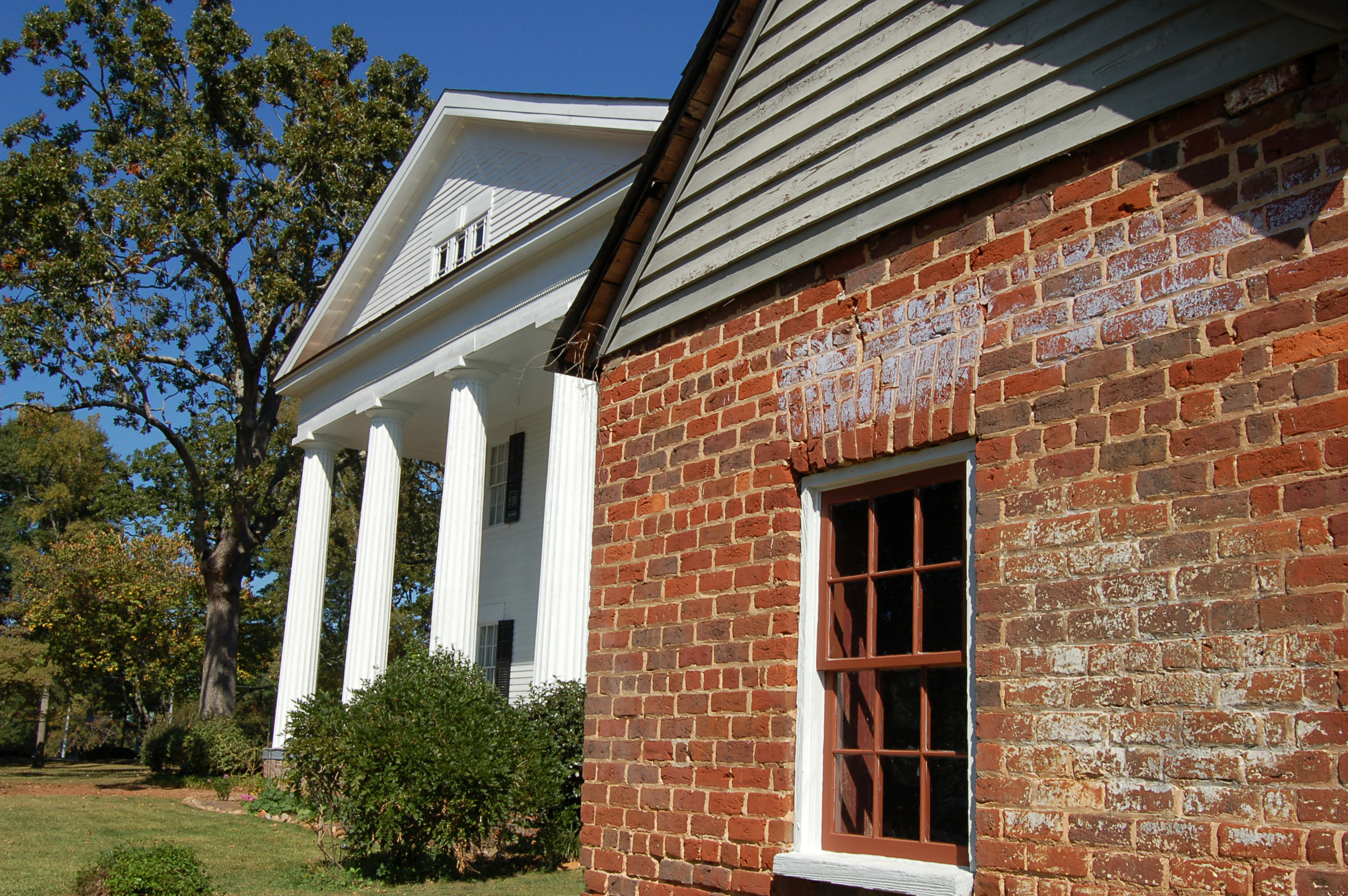 White Greek Revival building with Doric columns and a brick outbuilding on a green lawn.