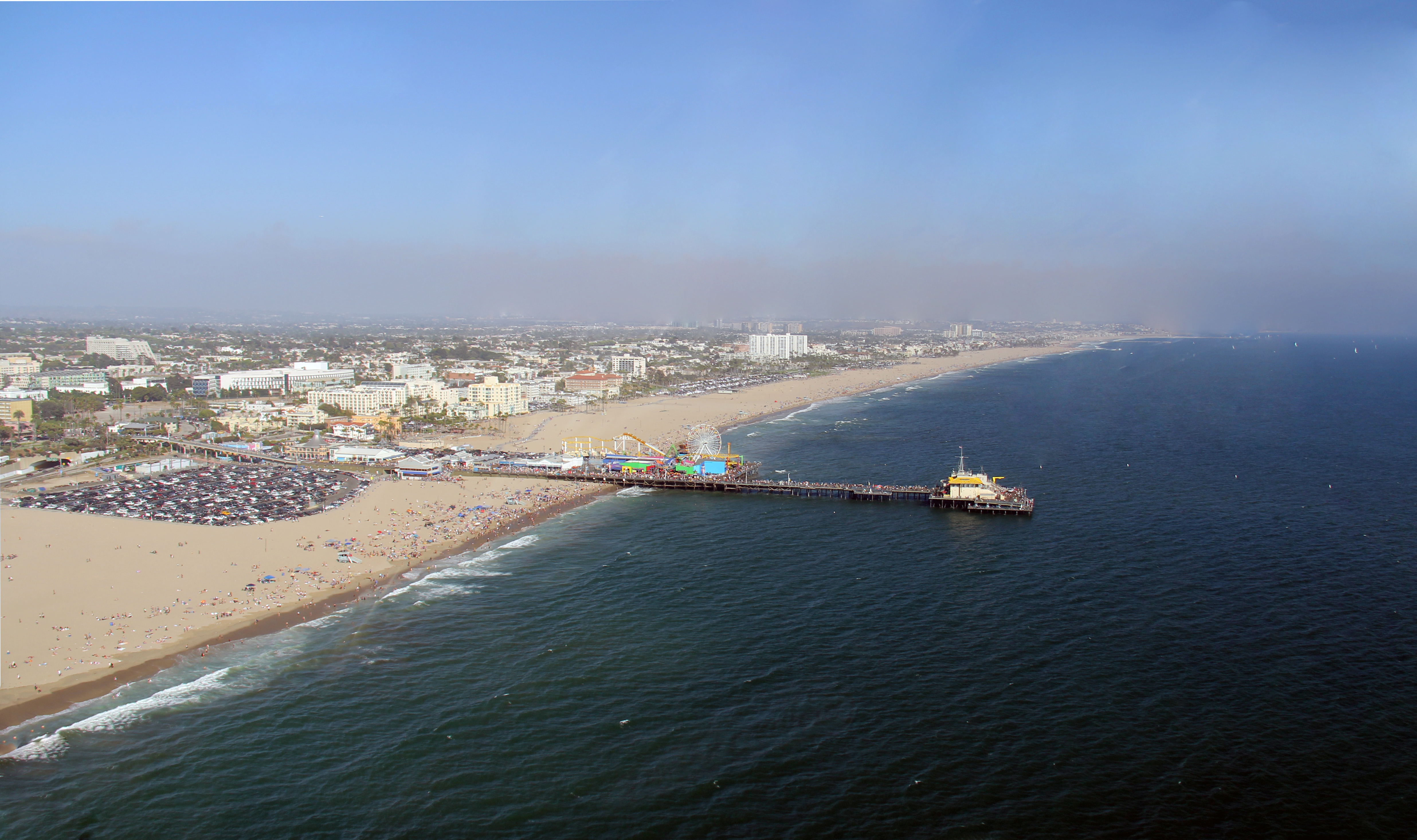 Aerial view of Santa Monica Beach and Pier stretching into the ocean with beachgoers on the sand.