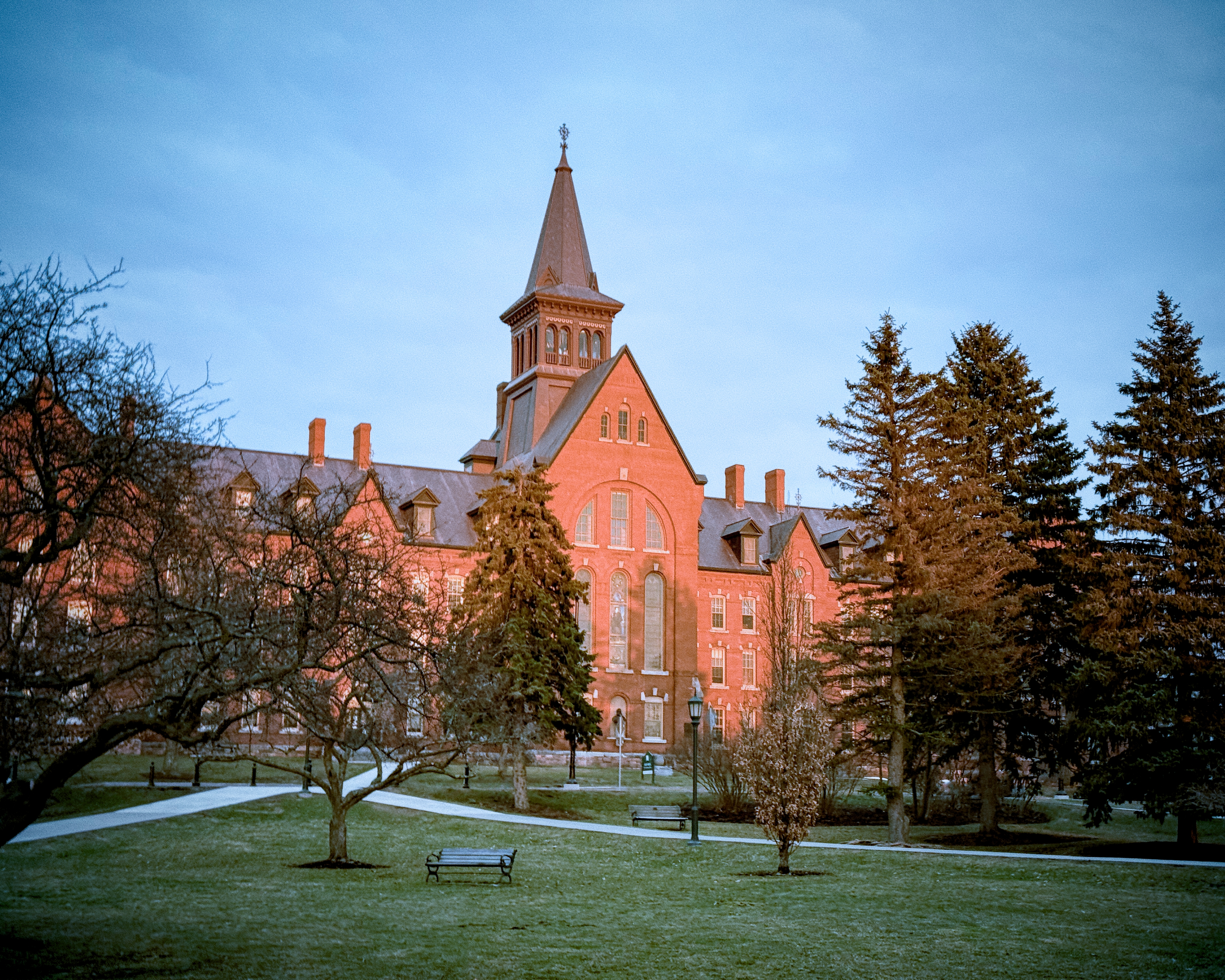 Historic red-brick building with a steeple on a frost-covered campus green in winter.