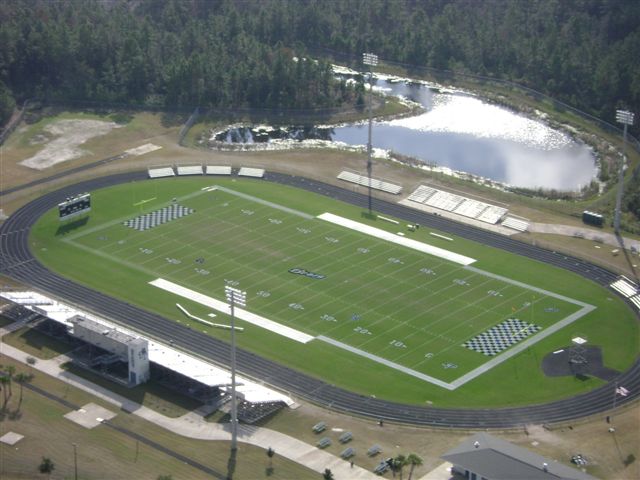 Aerial view of a high school football stadium with synthetic turf, running track, and light towers.