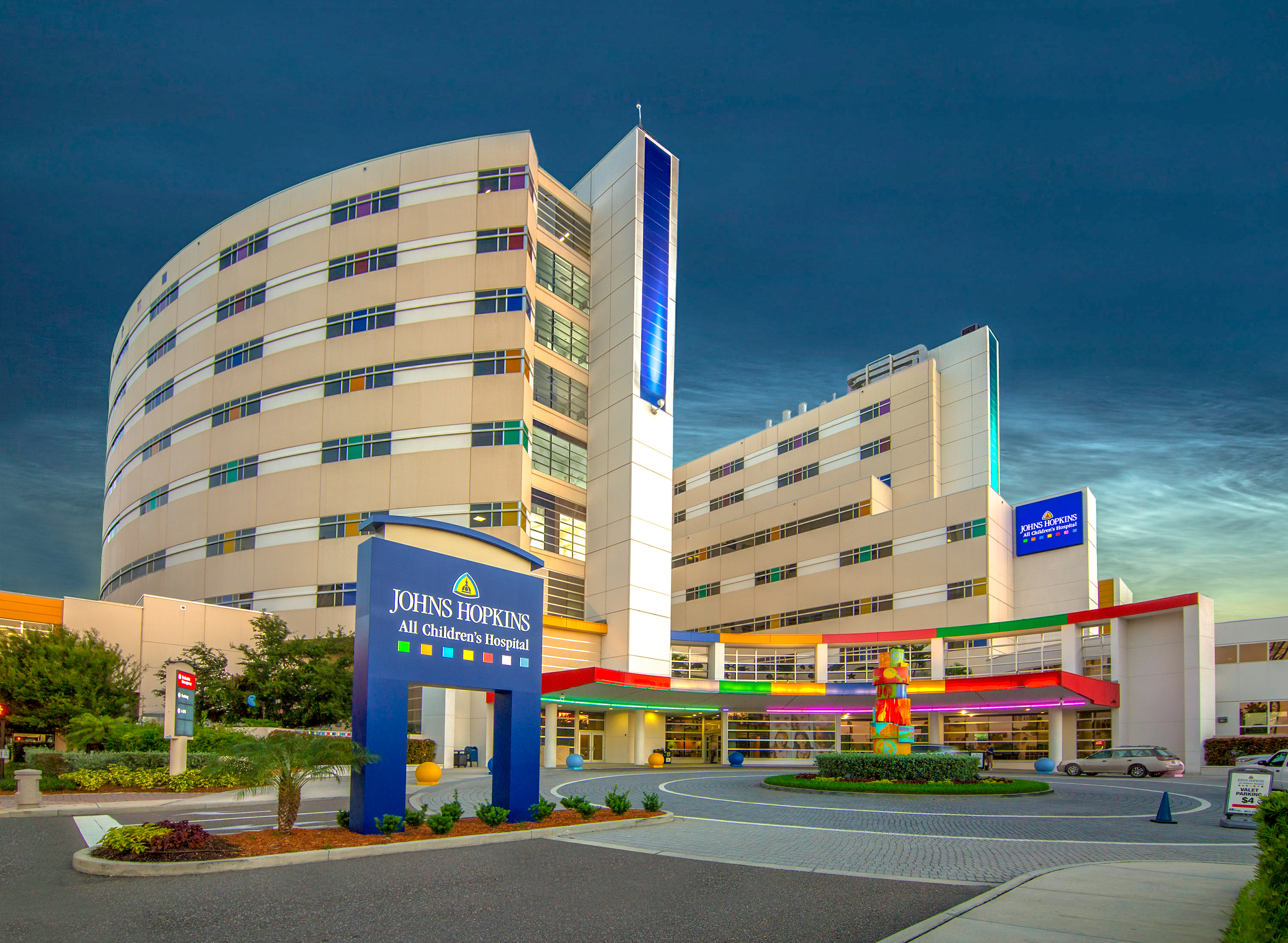 Multi-story hospital building with colorful facade and covered entrance at dusk.