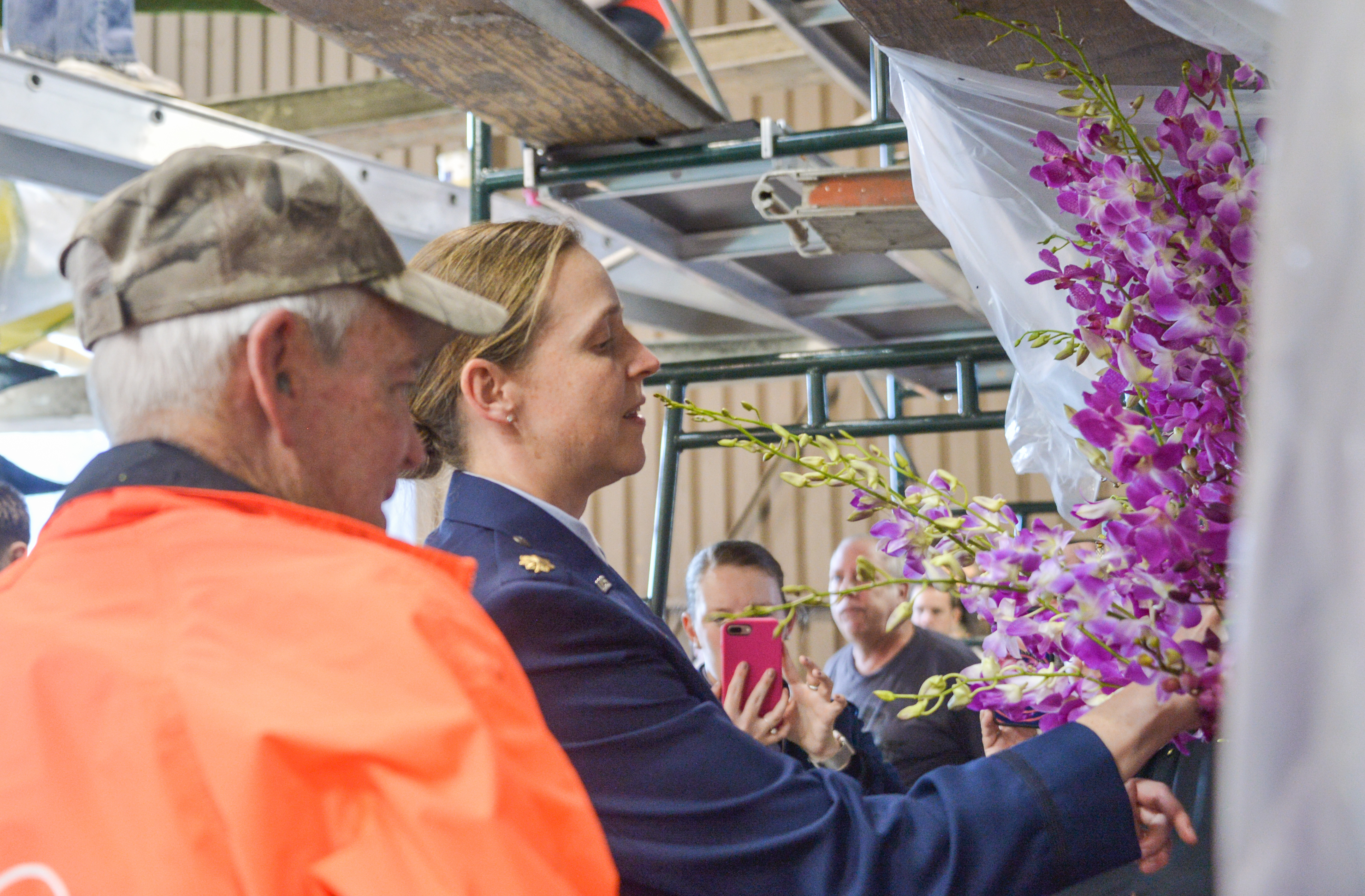 A person applies purple orchid flowers to a decorated Rose Parade float indoors.
