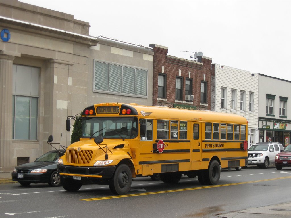 Yellow school bus driving down a street past commercial buildings.