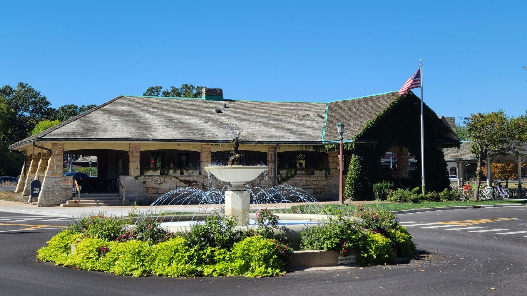 Stone and shingle civic building with a circular fountain and American flag out front.