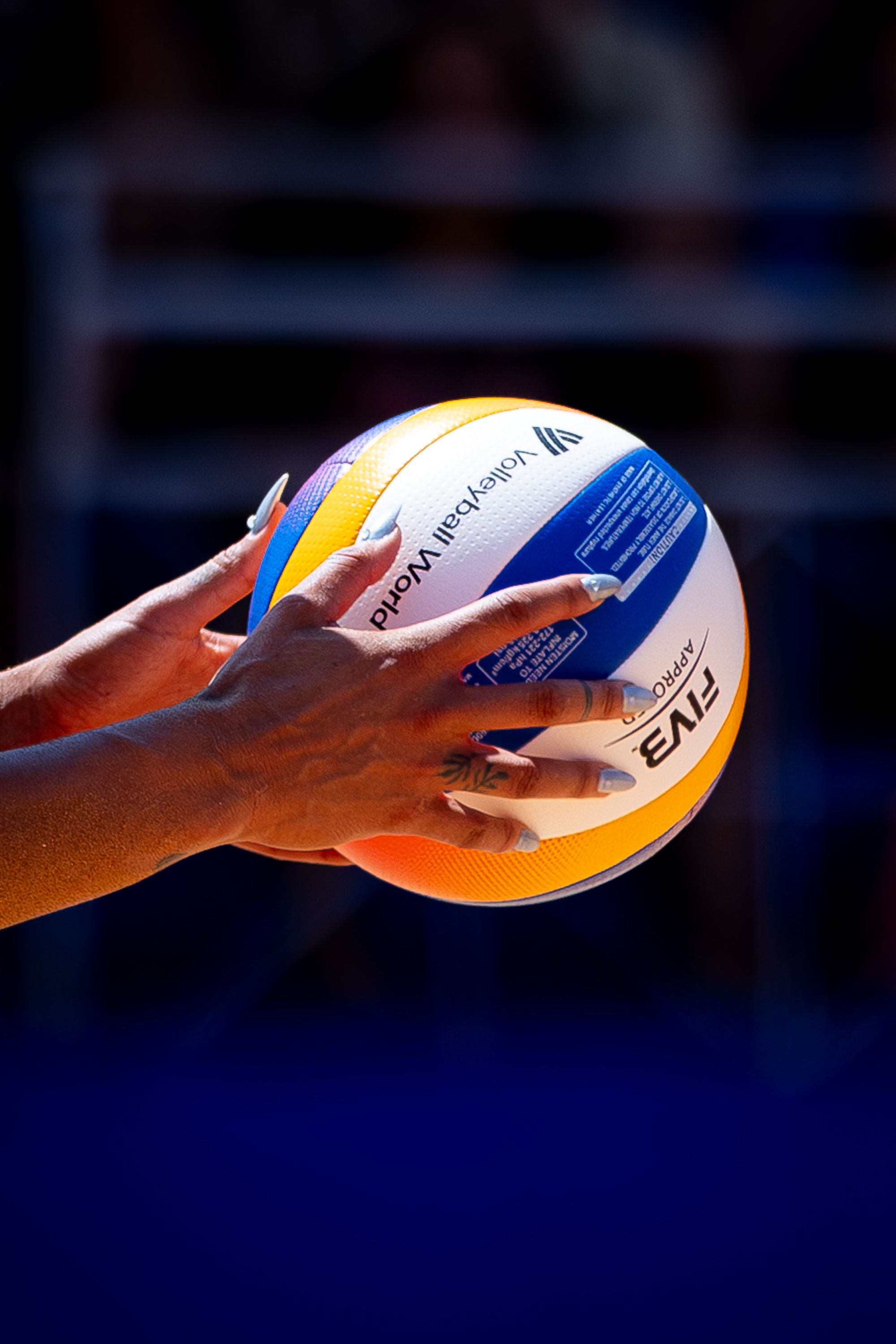 Close-up of hands gripping a colorful volleyball outside.