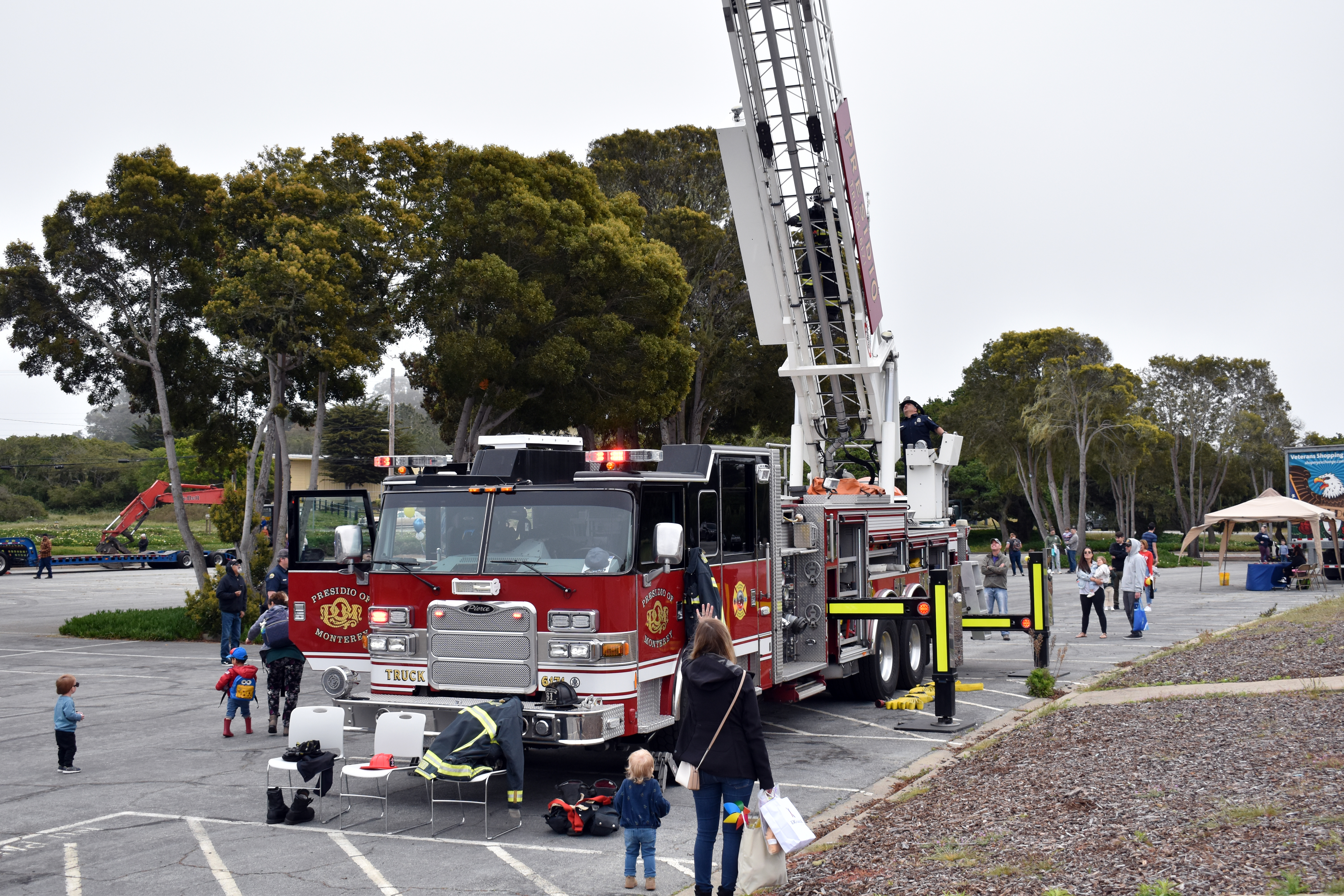 A red aerial ladder fire truck surrounded by children and adults at an outdoor event.