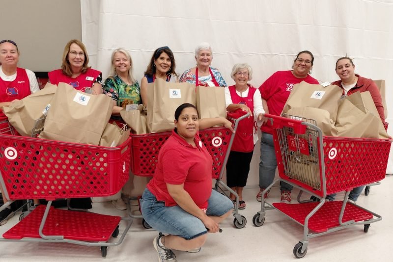 Group of women posing with red Target shopping carts filled with brown paper bags.