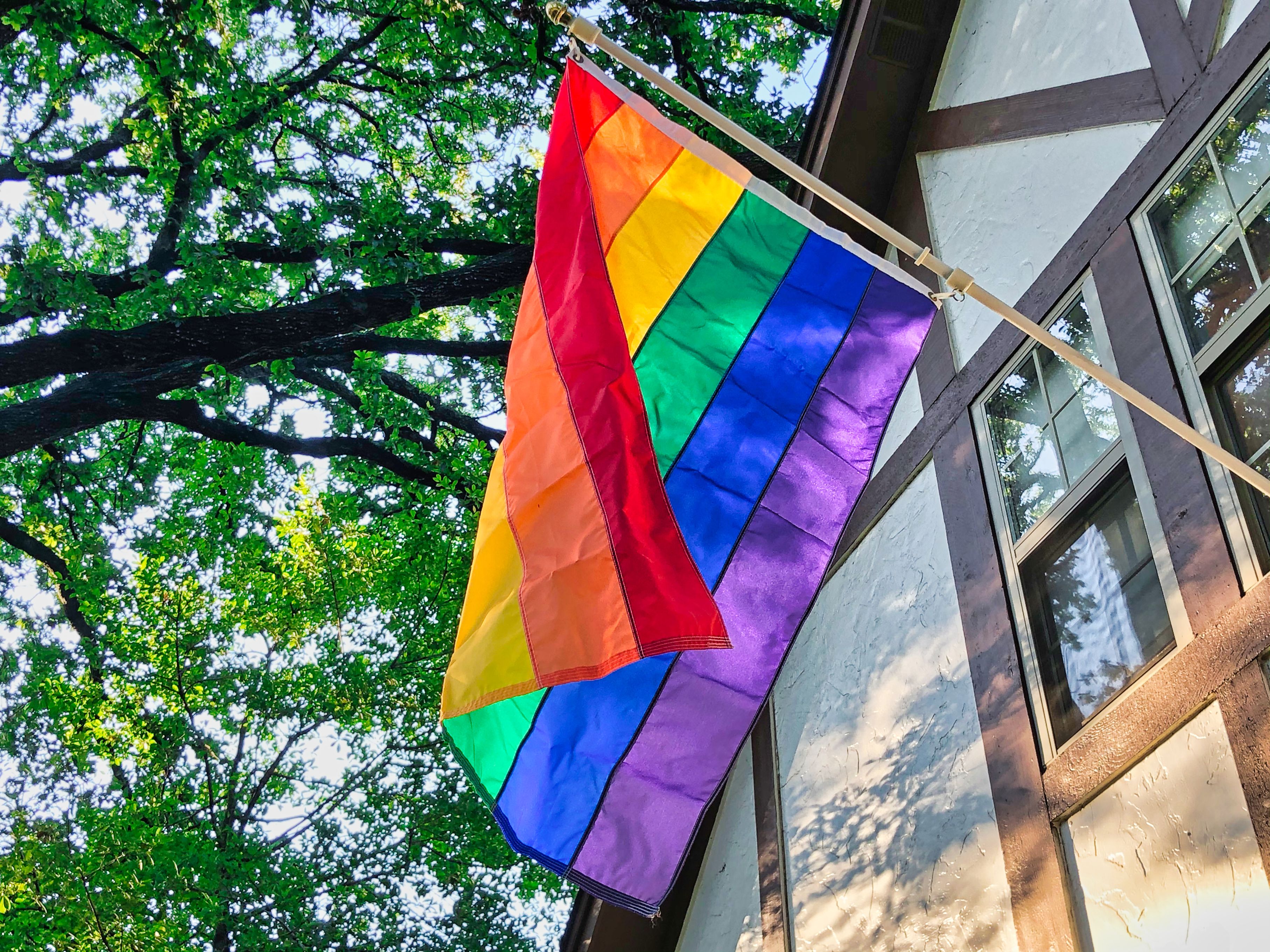 A rainbow pride flag mounted on a pole on the exterior of a building.