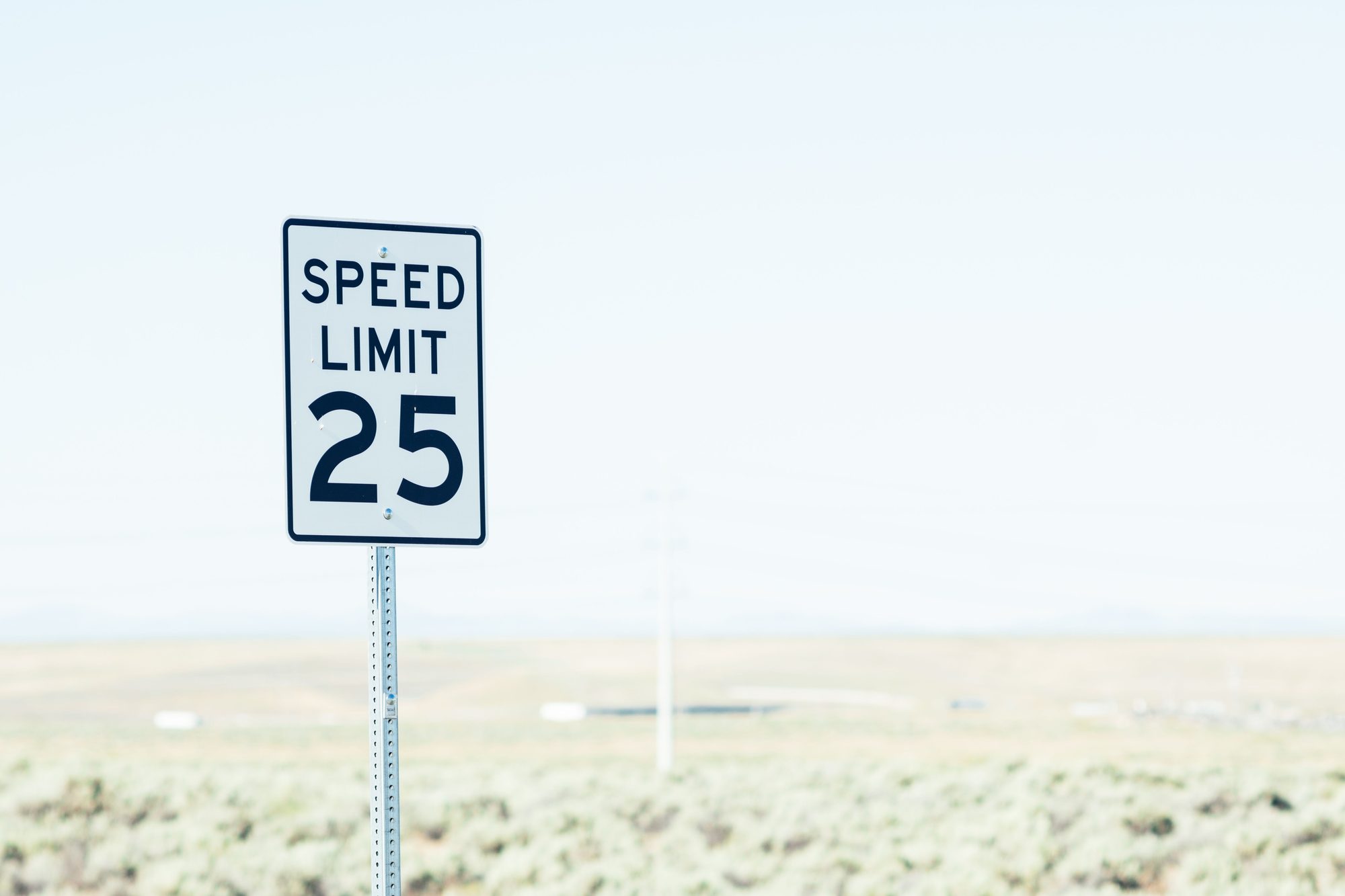 White sign on roadside with speed limit against empty green field at daytime