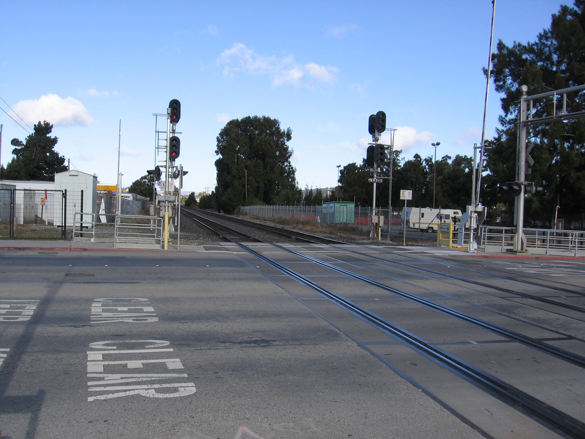 Railroad grade crossing with signal lights and yellow safety bollards beside train tracks.