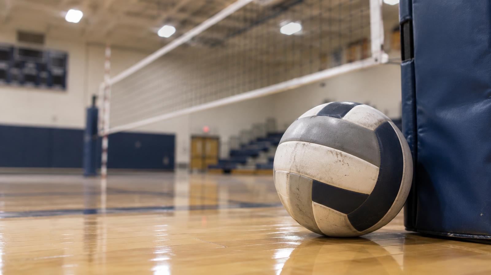 A volleyball resting on a gym floor next to a net post.