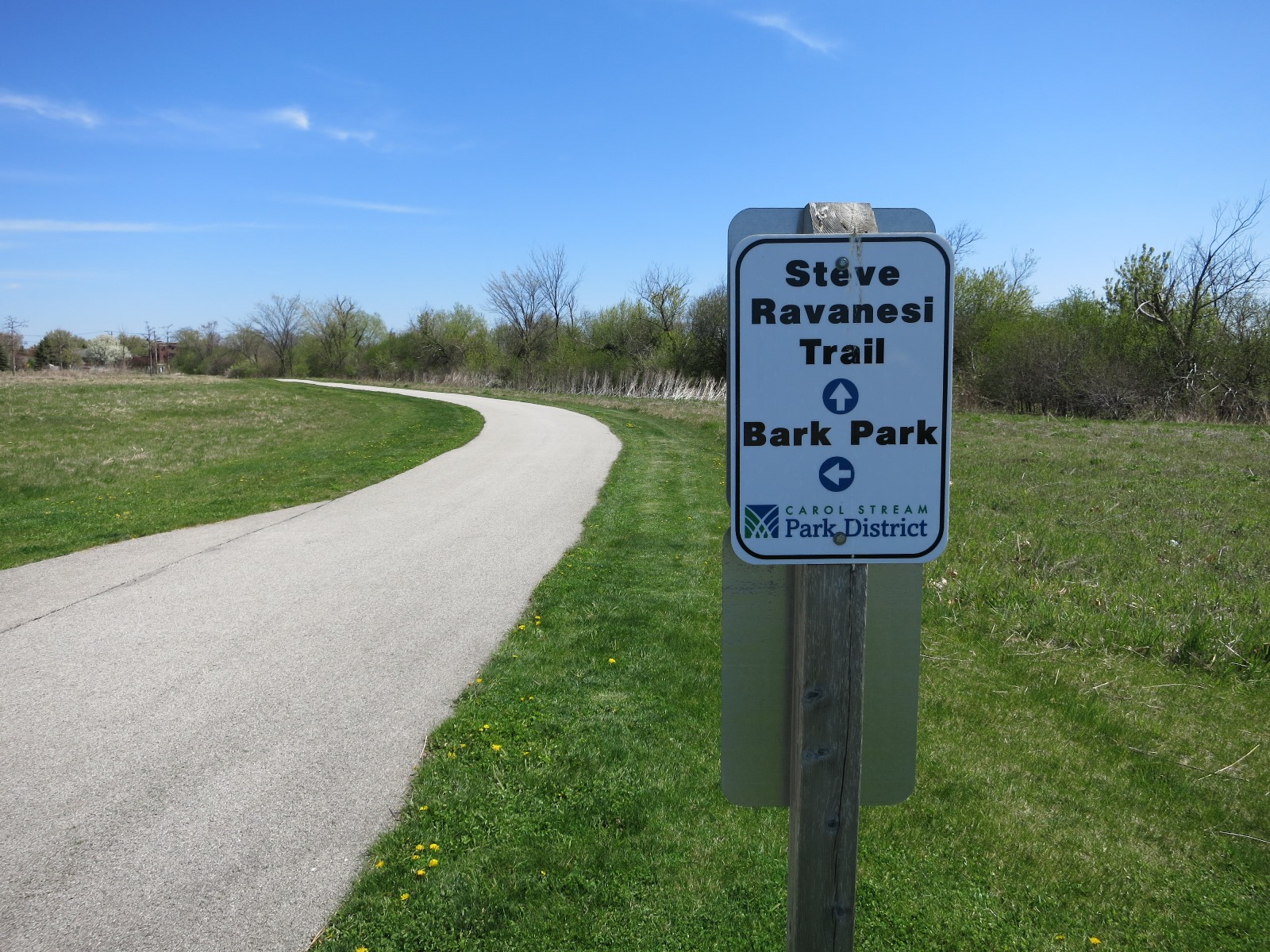 Sign for Carol Stream Park District's Steve Ravanesi Trail along a paved path.