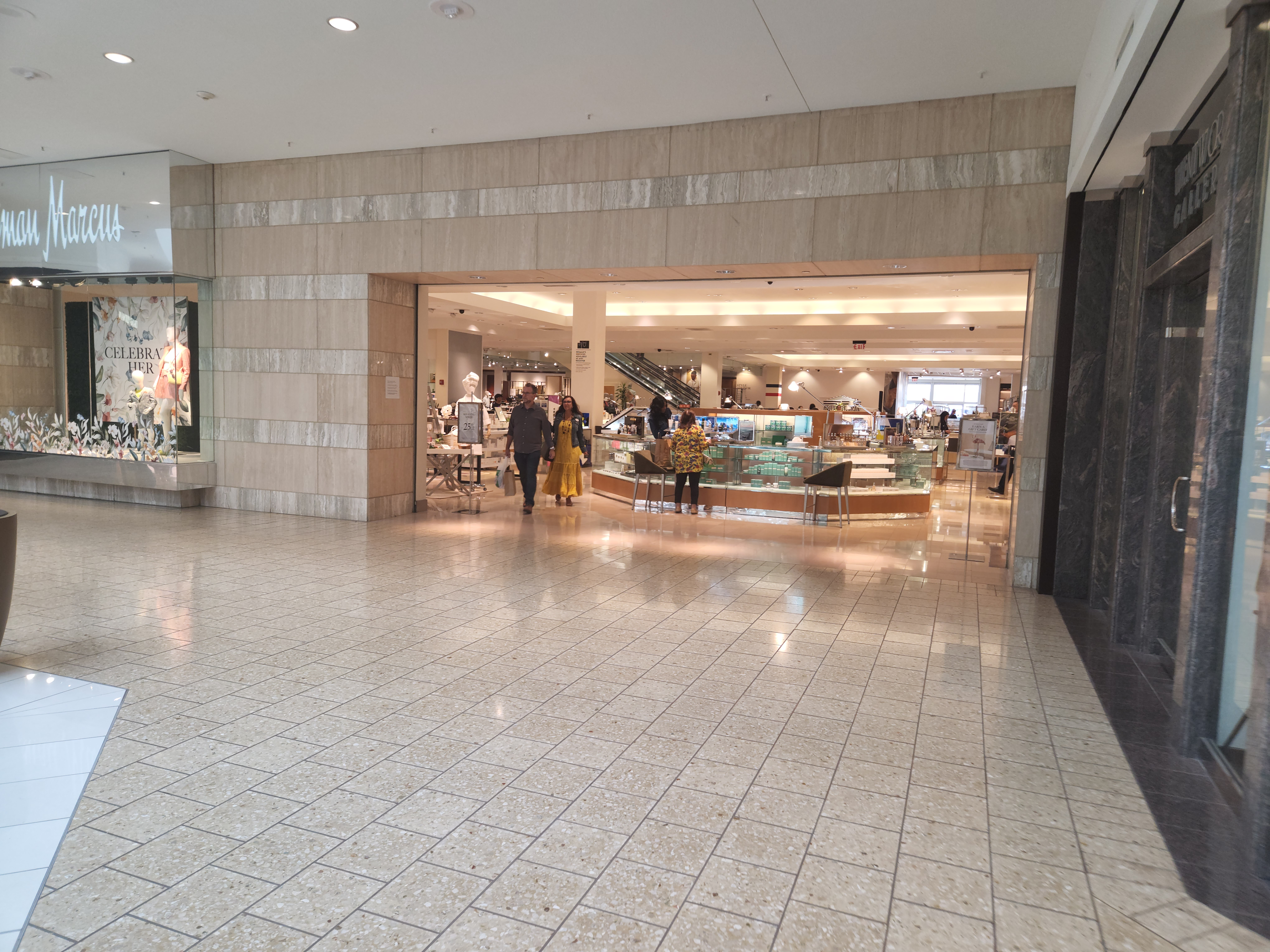 Polished tile corridor inside an upscale shopping mall with a department store entrance.