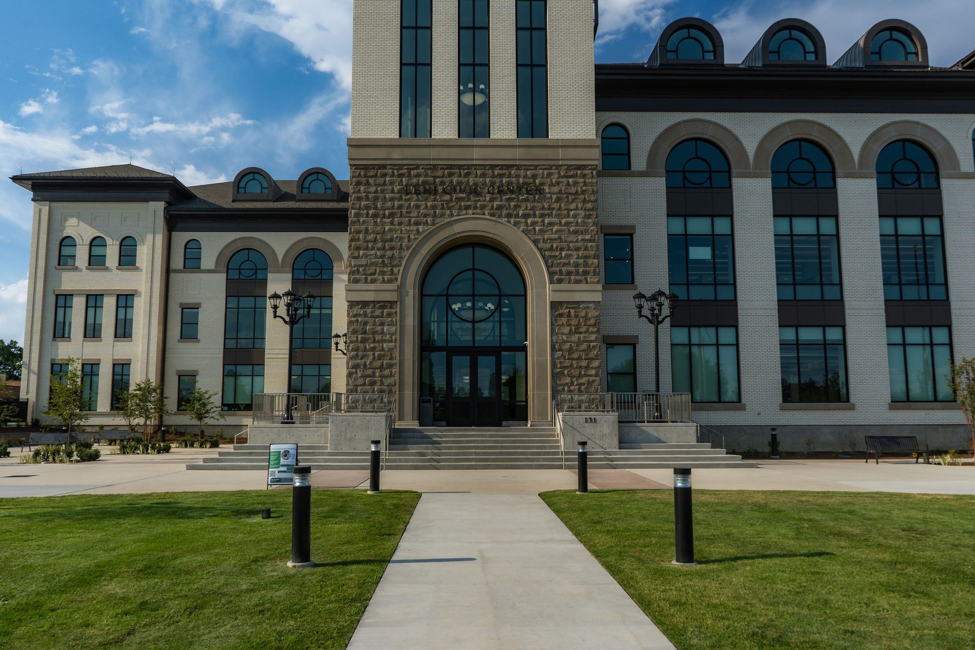 Neoclassical government building with stone arch entrance and green lawn on a sunny day.